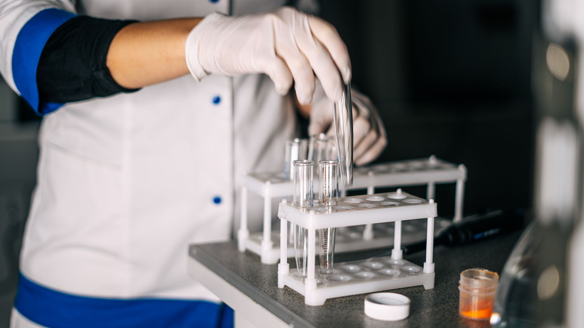rows of clinical trial laboratory benches with centrifuges, sample vials, and analytical equipment under bright white lighting in a pharmaceutical research facility