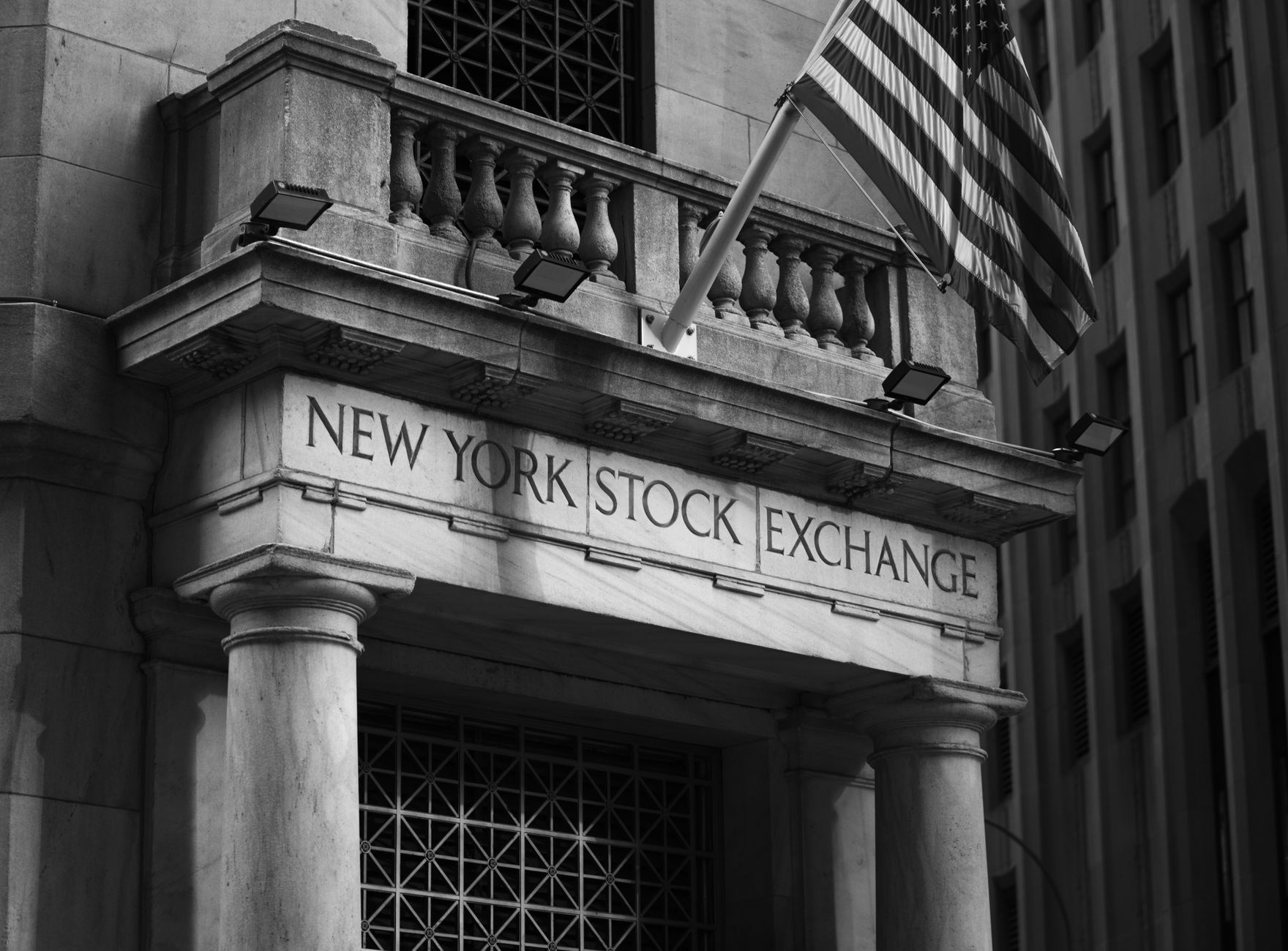 exterior of a stock exchange building at midday with a large digital ticker display mounted on the facade showing mixed market data
