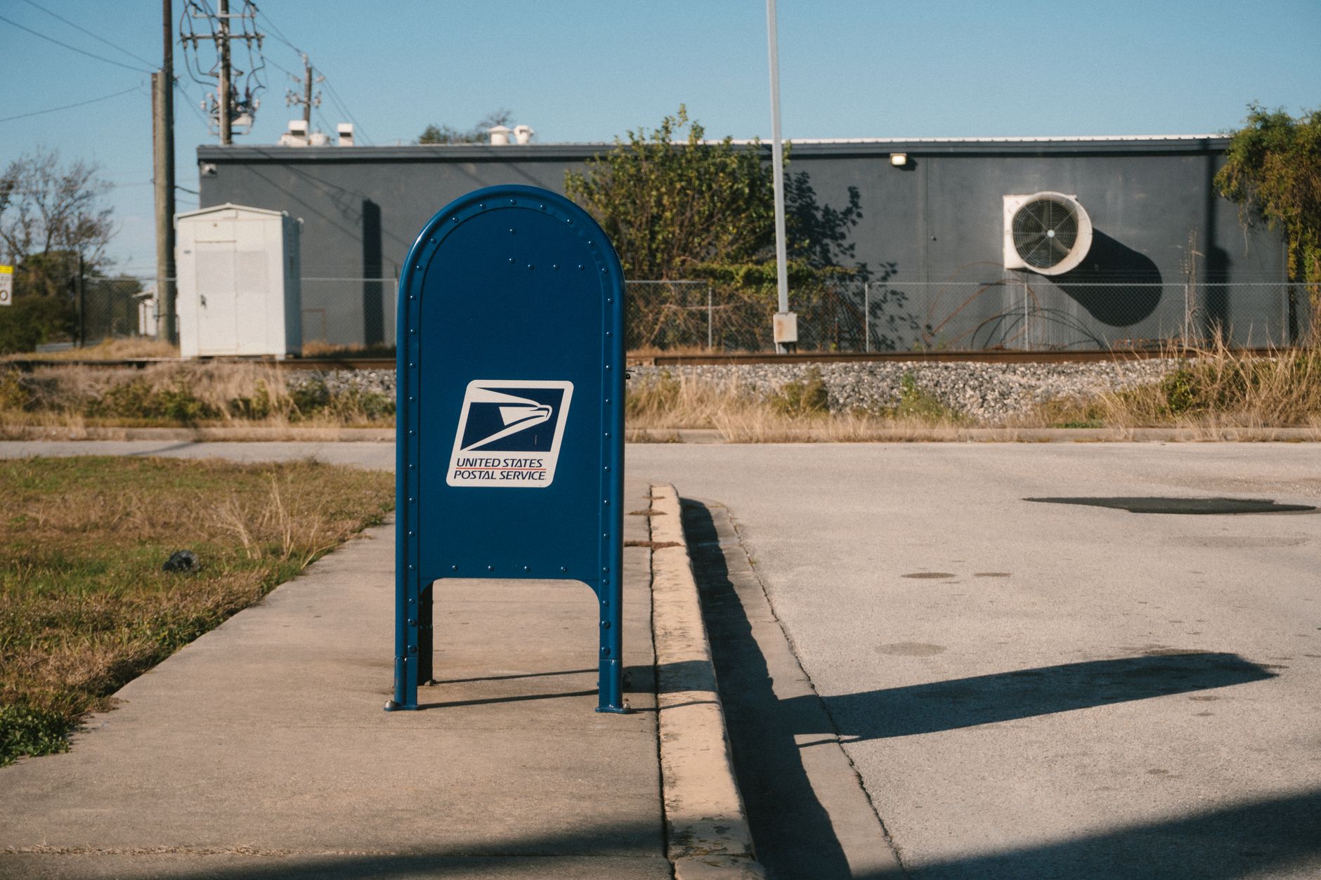 a weathered wooden mailbox mounted near a rural road with an overflowing stack of government benefit envelopes visible inside