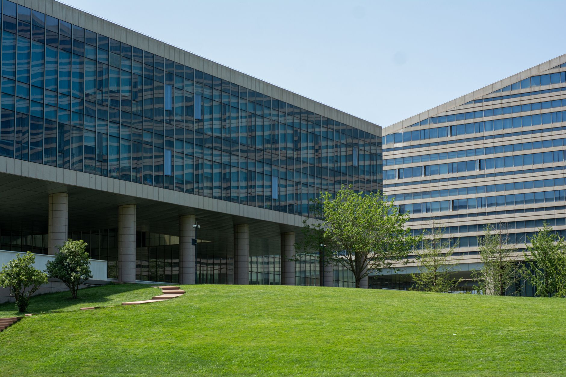 exterior of a modern biotech research facility with glass facades reflecting a clear sky, set against a suburban office park landscape