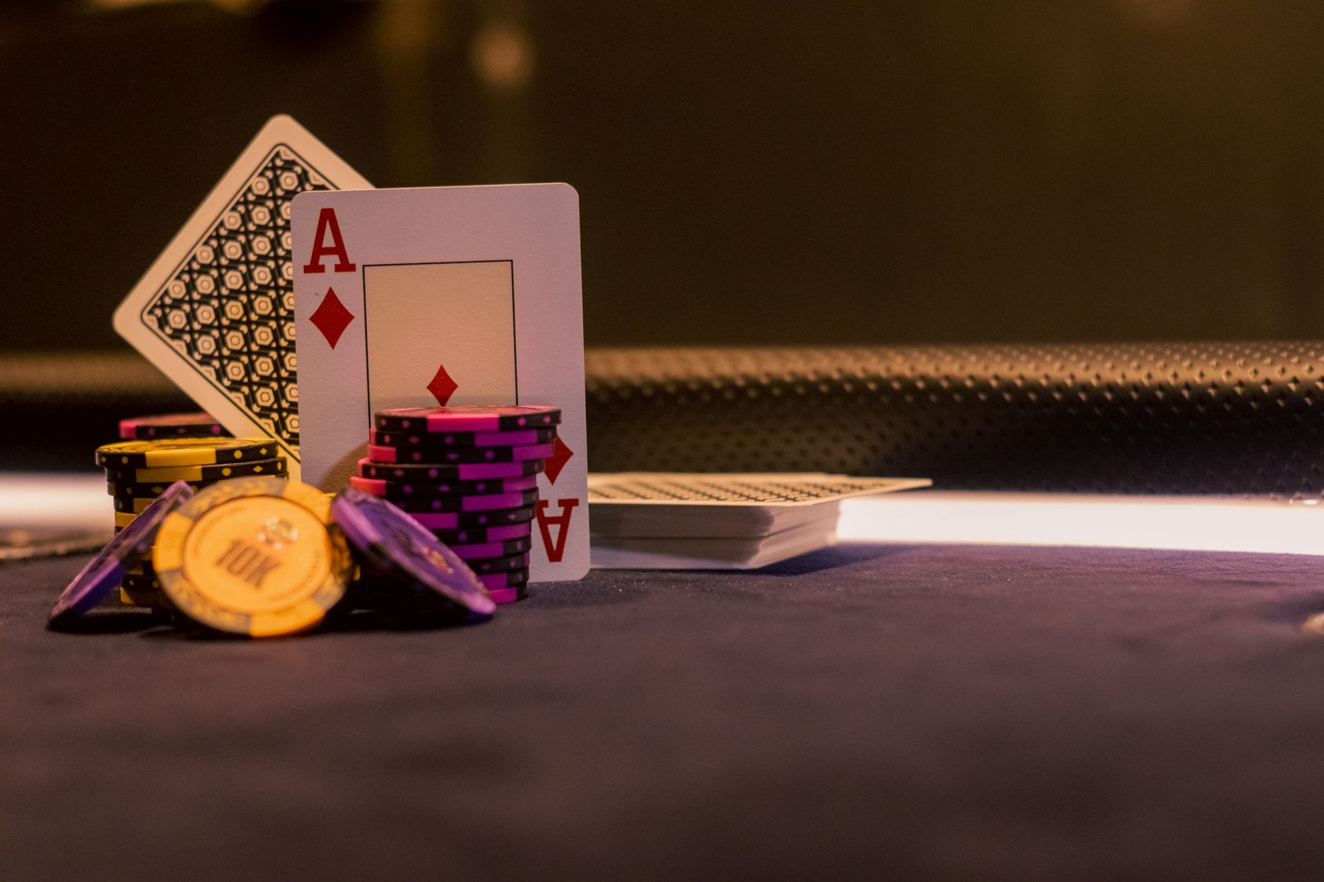 rows of empty casino table gaming stations in a softly lit, high-ceilinged casino floor, green felt surfaces visible with no players present