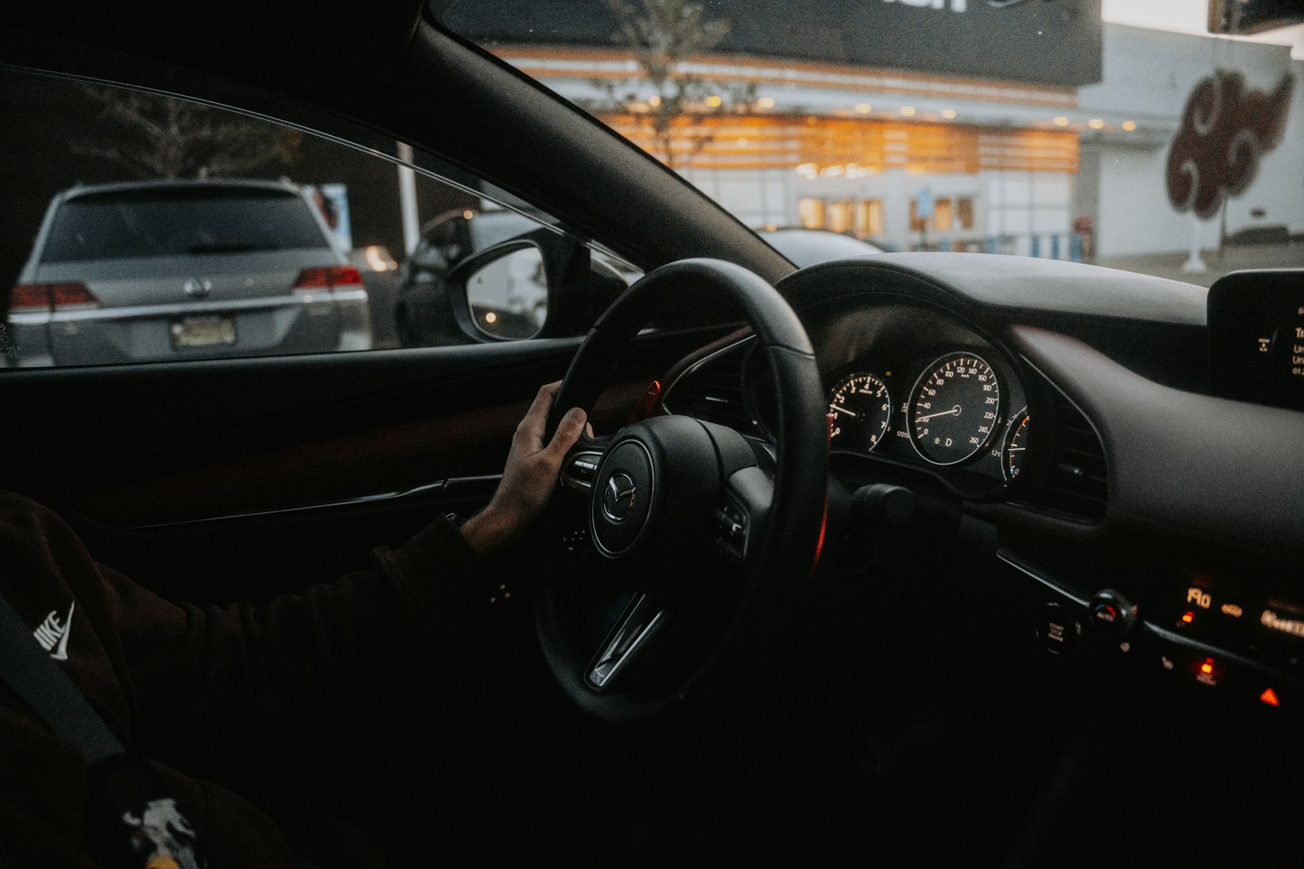 close-up of a cracked windshield on a parked sedan in a rental car lot, repair estimate paperwork visible on the dashboard