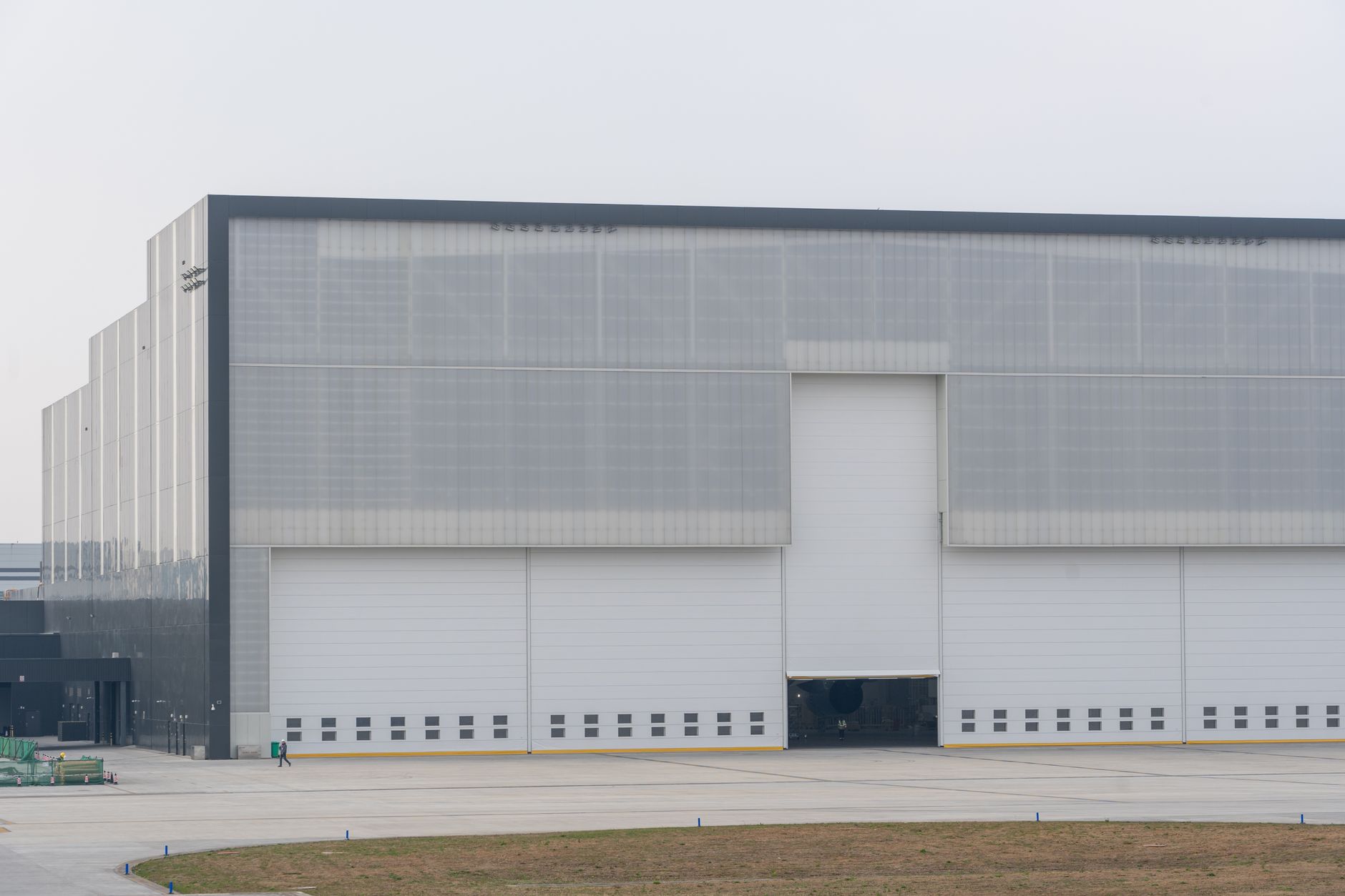 exterior of a large semiconductor fabrication facility at early morning, industrial smokestacks and clean-room modules visible against a pale sky