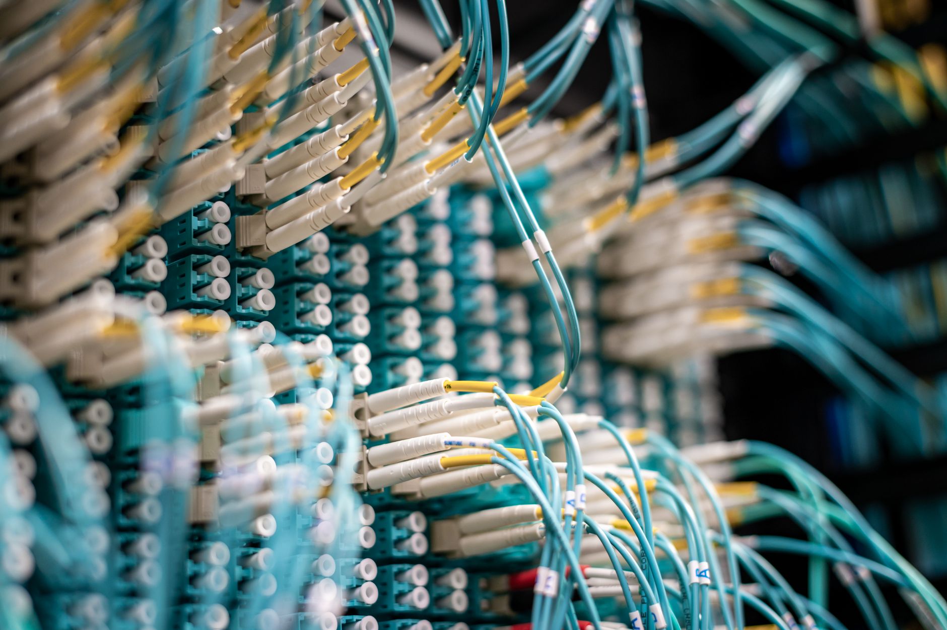 rows of illuminated server racks inside a large data center facility, fiber optic cables running along cable trays under blue ambient lighting
