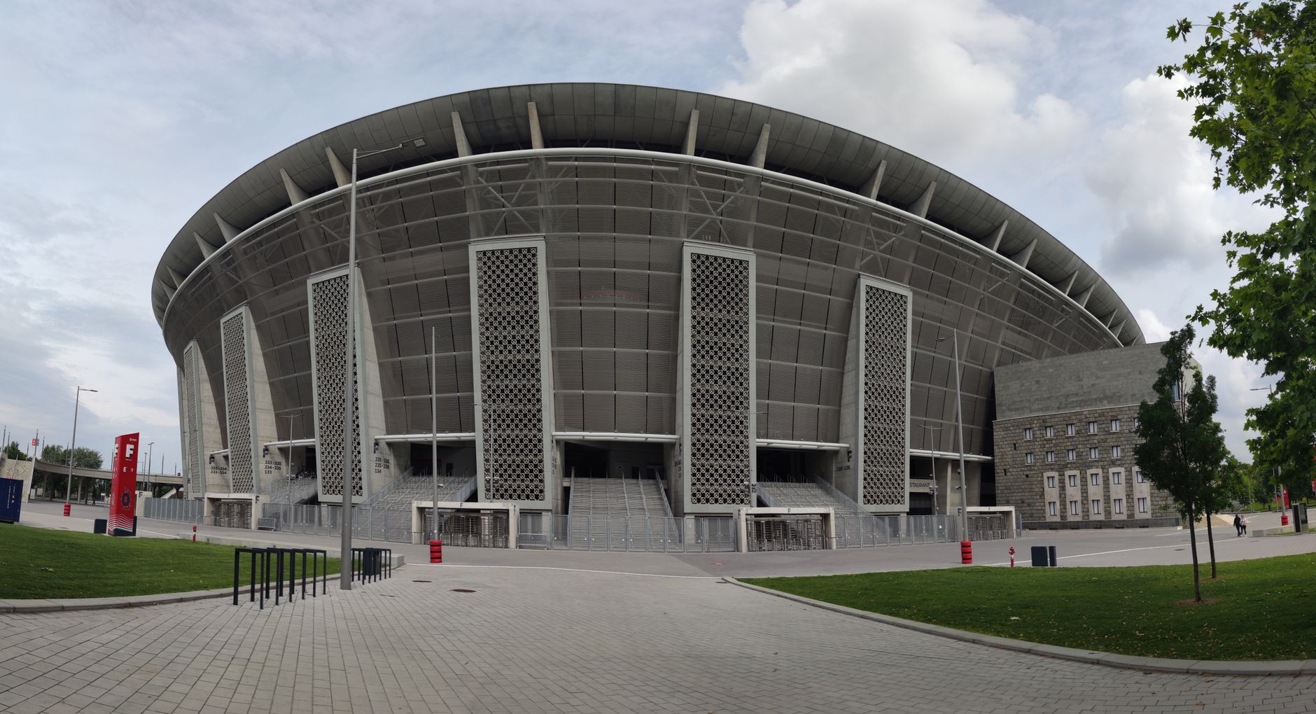 exterior view of Anfield stadium on a cloudy afternoon, red facade visible with empty forecourt and turnstiles in foreground
