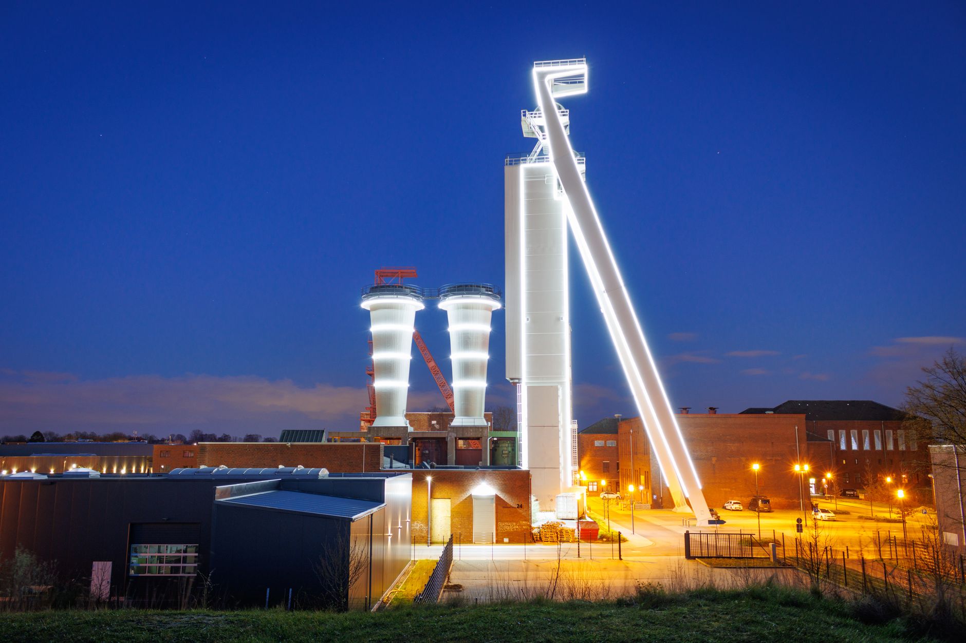 exterior of a semiconductor fabrication facility with clean room warning signs visible through glass, industrial equipment in the background at dusk