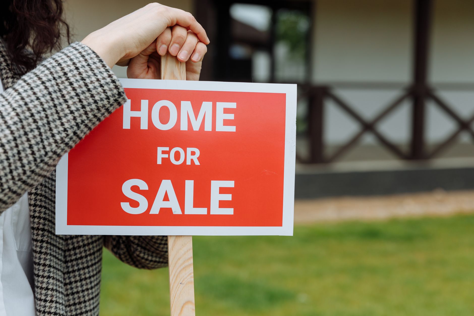 close-up of a residential real estate listing sign planted in a front lawn with a sold sticker attached, in a tree-lined street