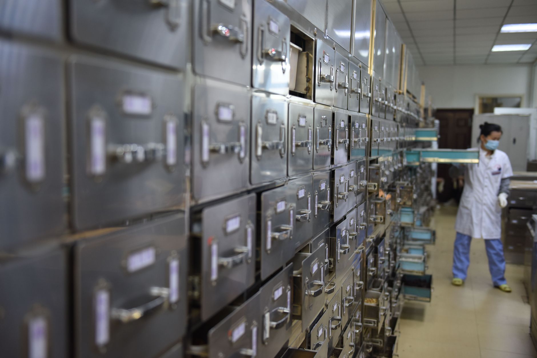 rows of labeled medicine storage shelves in a Nigerian hospital pharmacy, many slots visibly empty