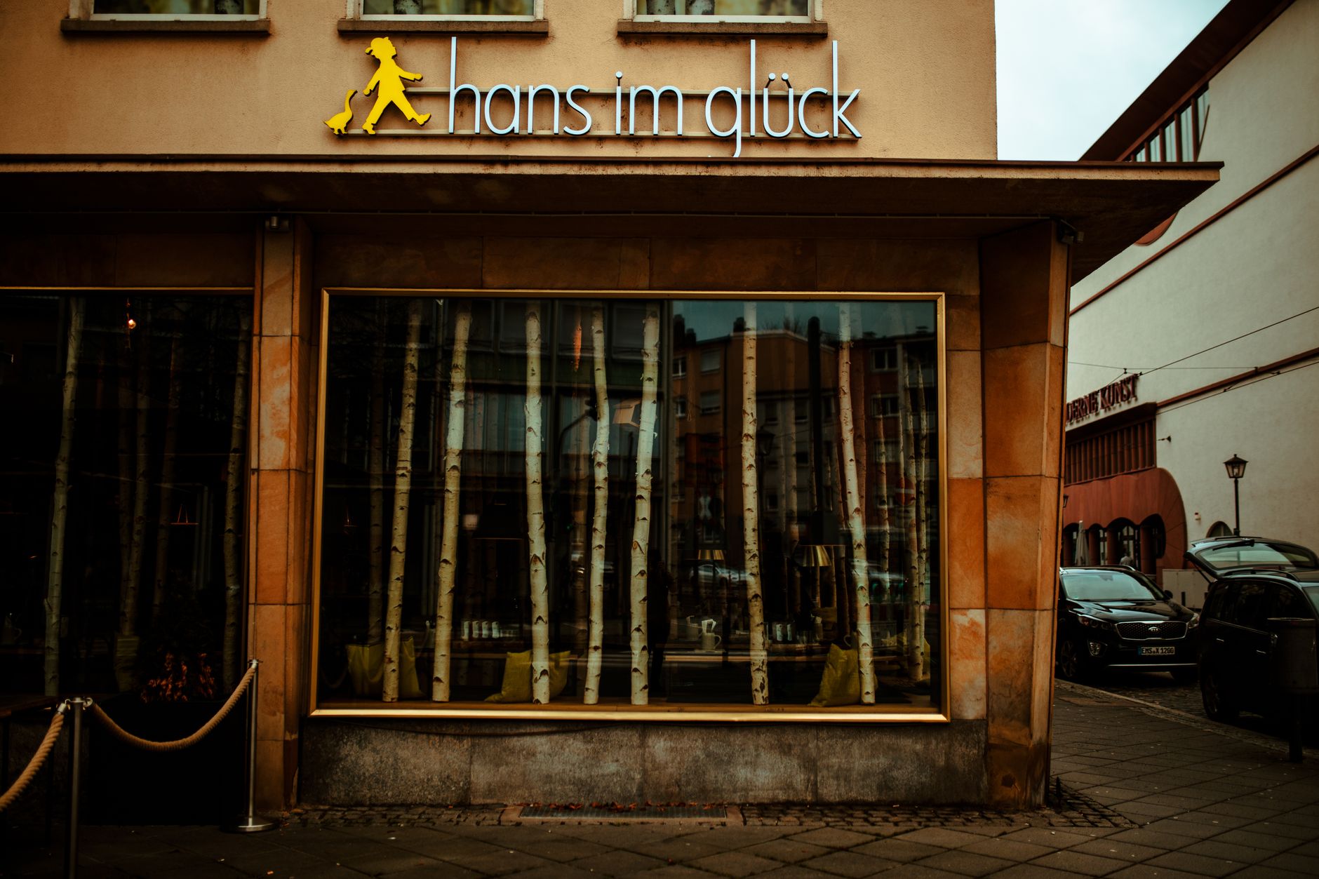 exterior of a mid-sized bank branch building on a quiet urban street, its signage reflecting afternoon light, with closed shutters on adjacent storefronts suggesting economic inactivity