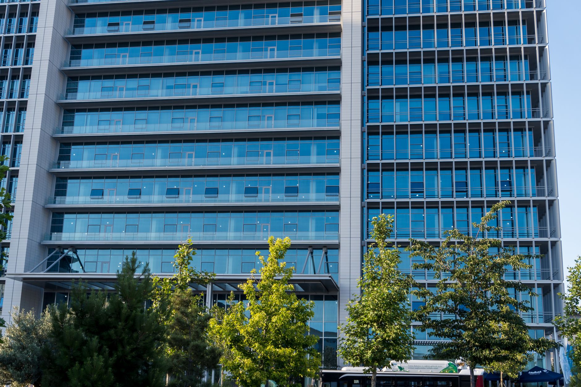 exterior of a modern glass-fronted financial technology office building at midday, with a street-level sign visible in the foreground