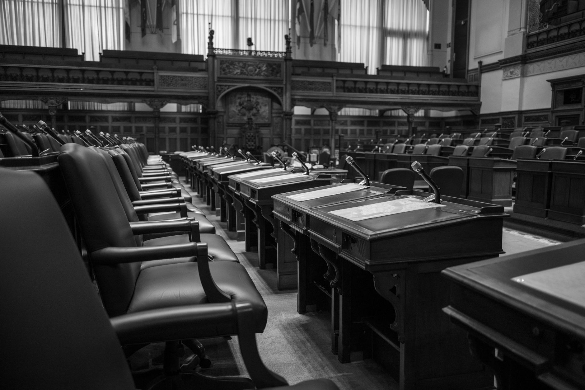interior of a state capitol building's legislative chamber, empty wooden desks arranged in a semicircle beneath a domed ceiling with natural light filtering through ornate windows