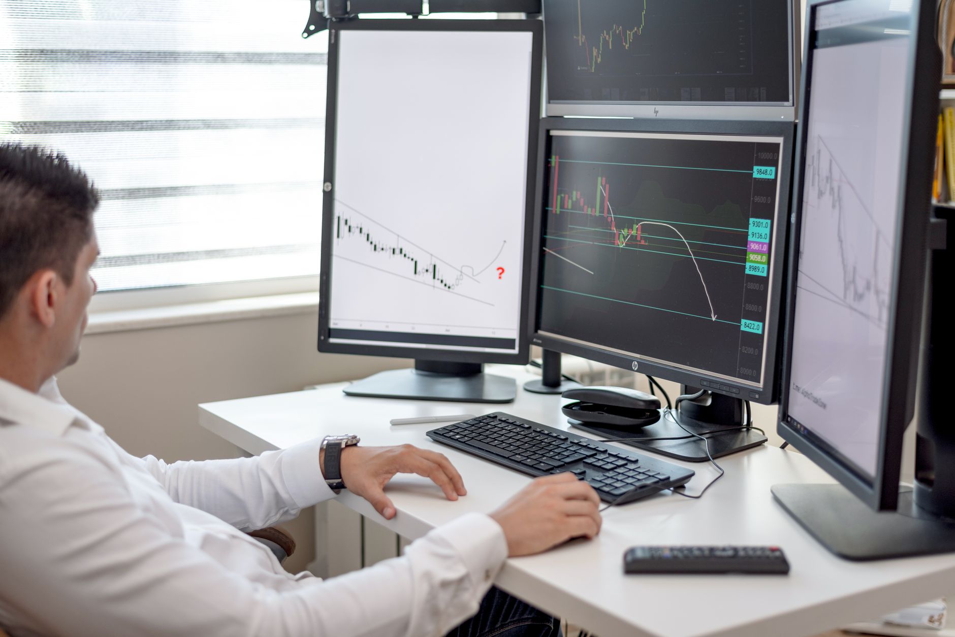 a close-up view of a multi-monitor trading workstation displaying futures order grids and margin balance readouts, keyboards and cable management visible in the background