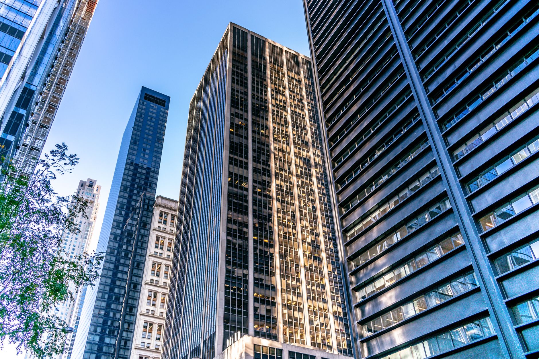 exterior of a large stone and glass financial district building at midday with empty plaza and a row of closed market stalls in the foreground