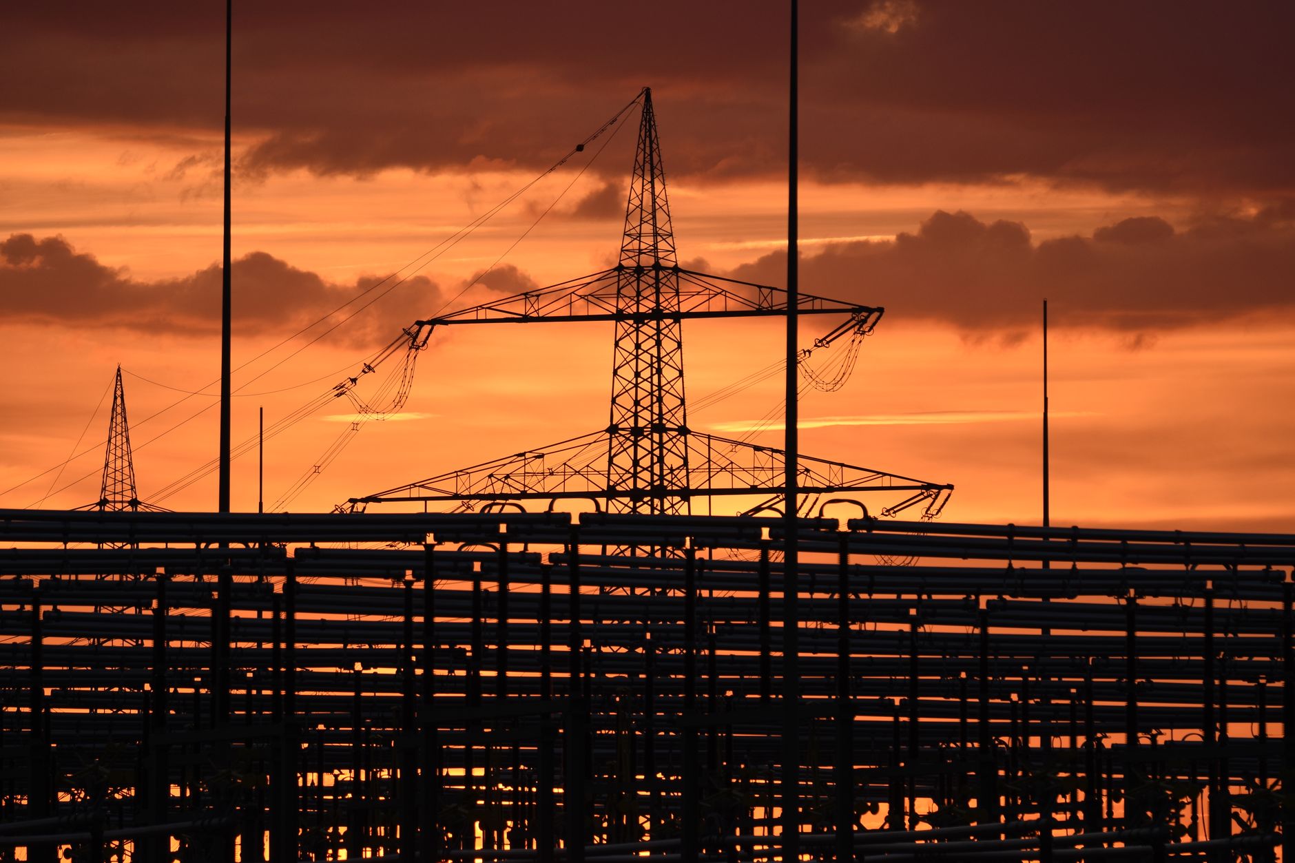 exterior of a large hyperscale data center building surrounded by high-voltage power transmission lines at dusk, set against an open rural landscape
