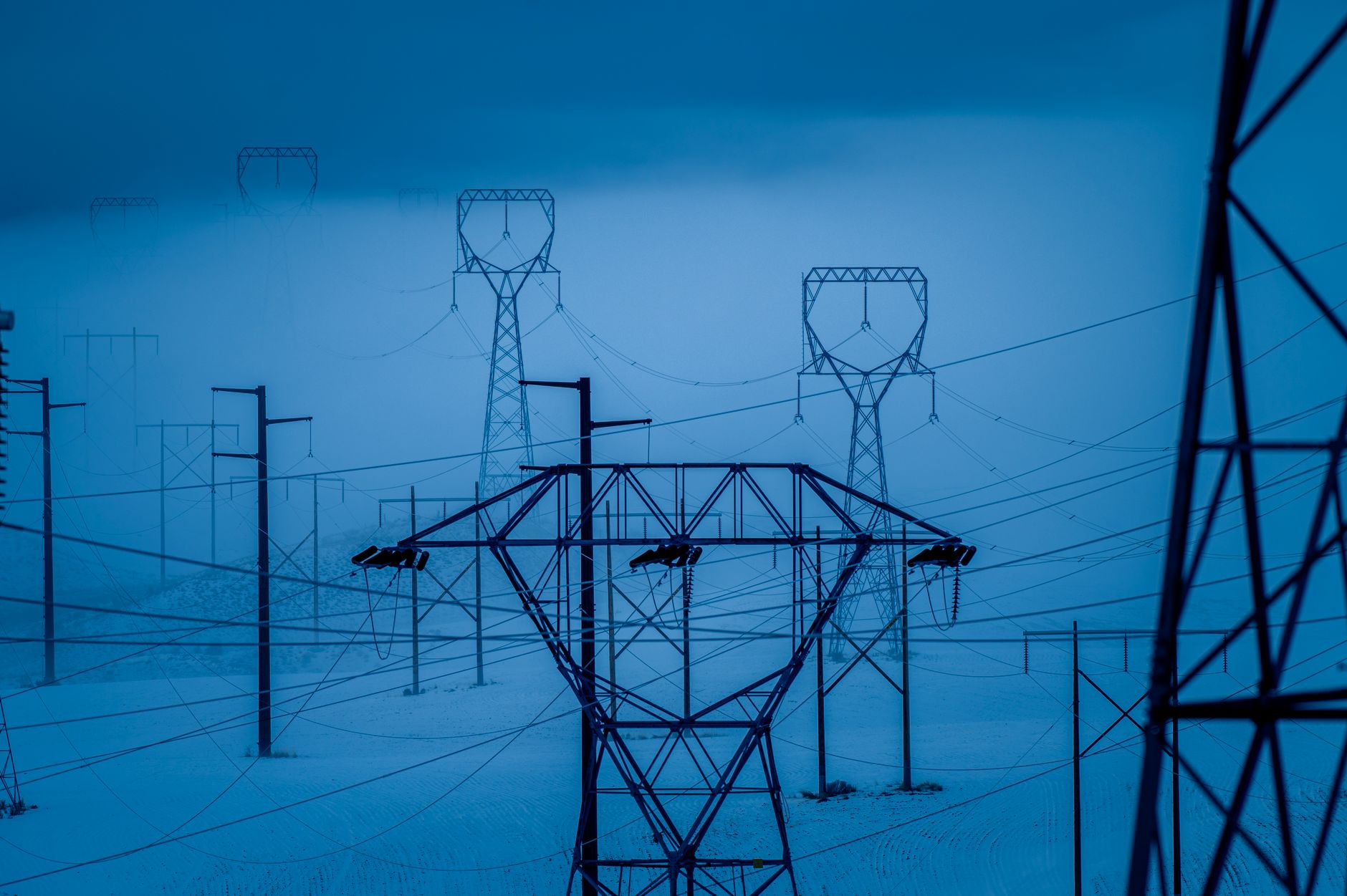 rows of industrial electricity transformers and switching equipment inside a utility substation, heavy cables visible overhead