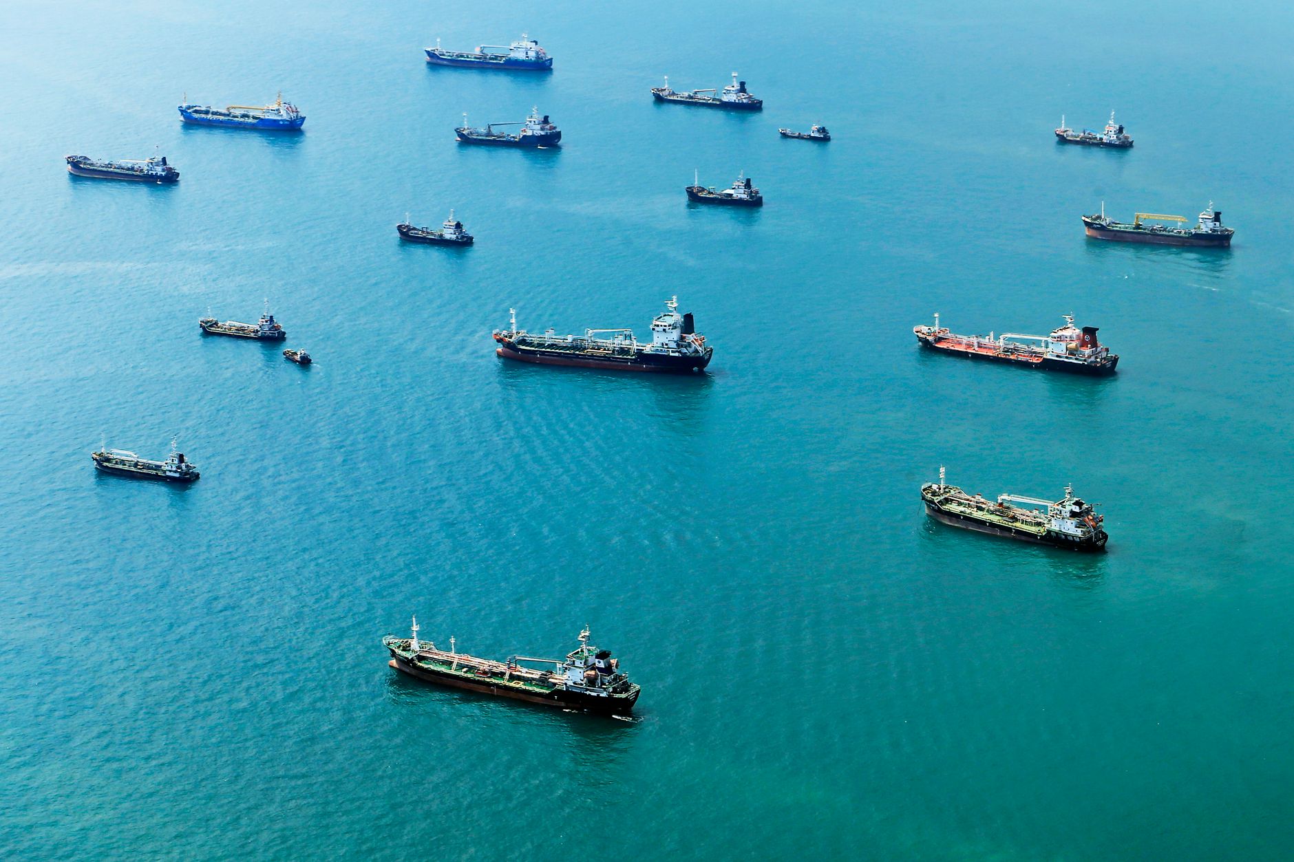 aerial view of oil tankers navigating a narrow strait at dusk, ocean surface reflecting orange light