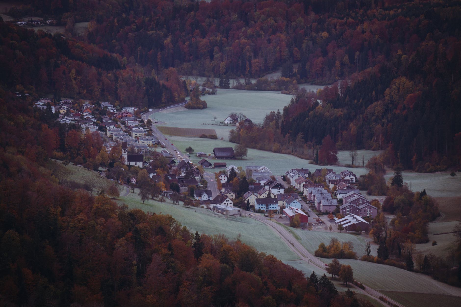 a wide aerial view of a rural West Virginia town nestled between forested Appalachian ridgelines, with a mix of older homes and newer residential construction visible along a river valley road