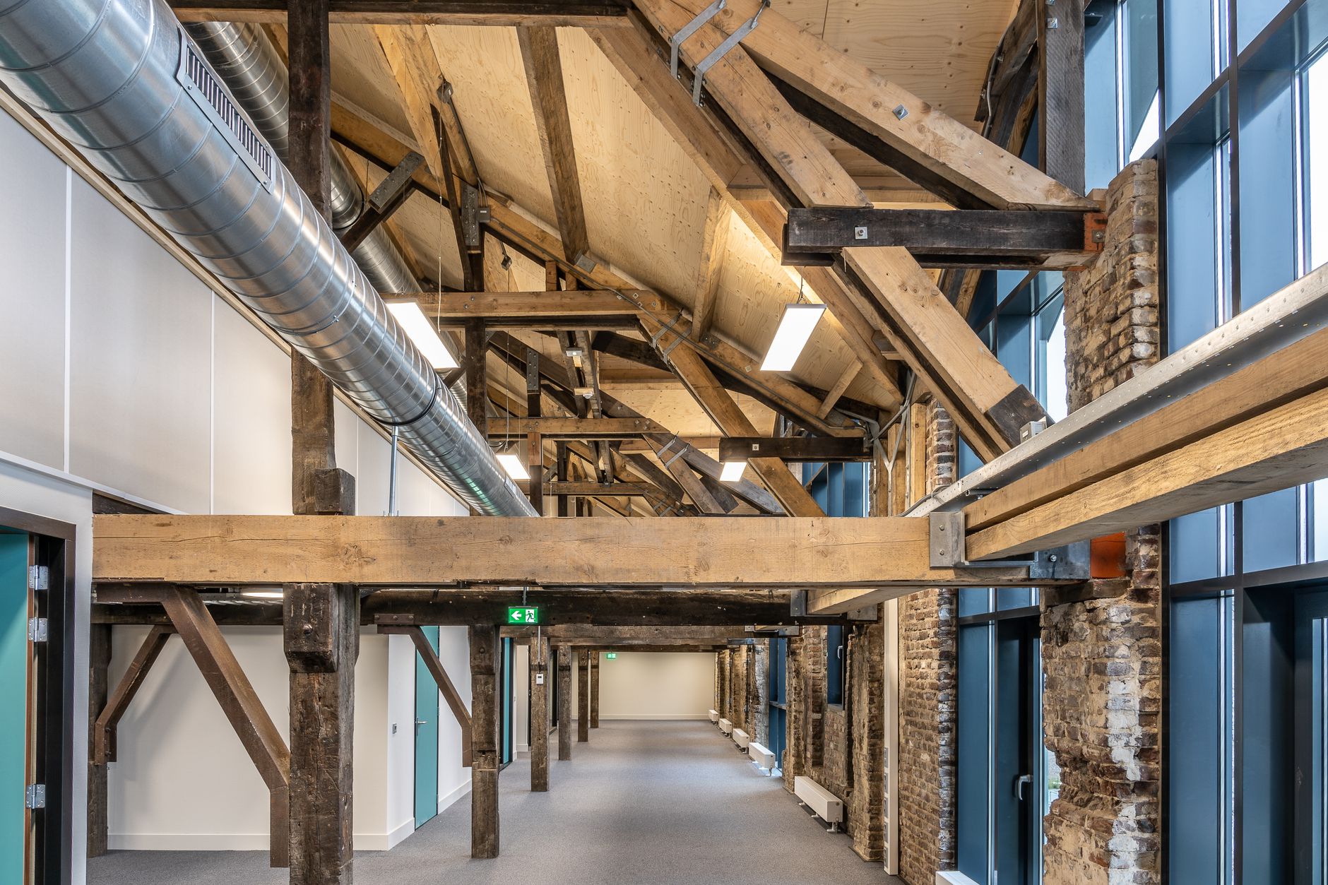interior of a modern coworking space in a converted historic brick building, with exposed wooden beams, rows of desks with open laptops, and large windows overlooking a small-town main street