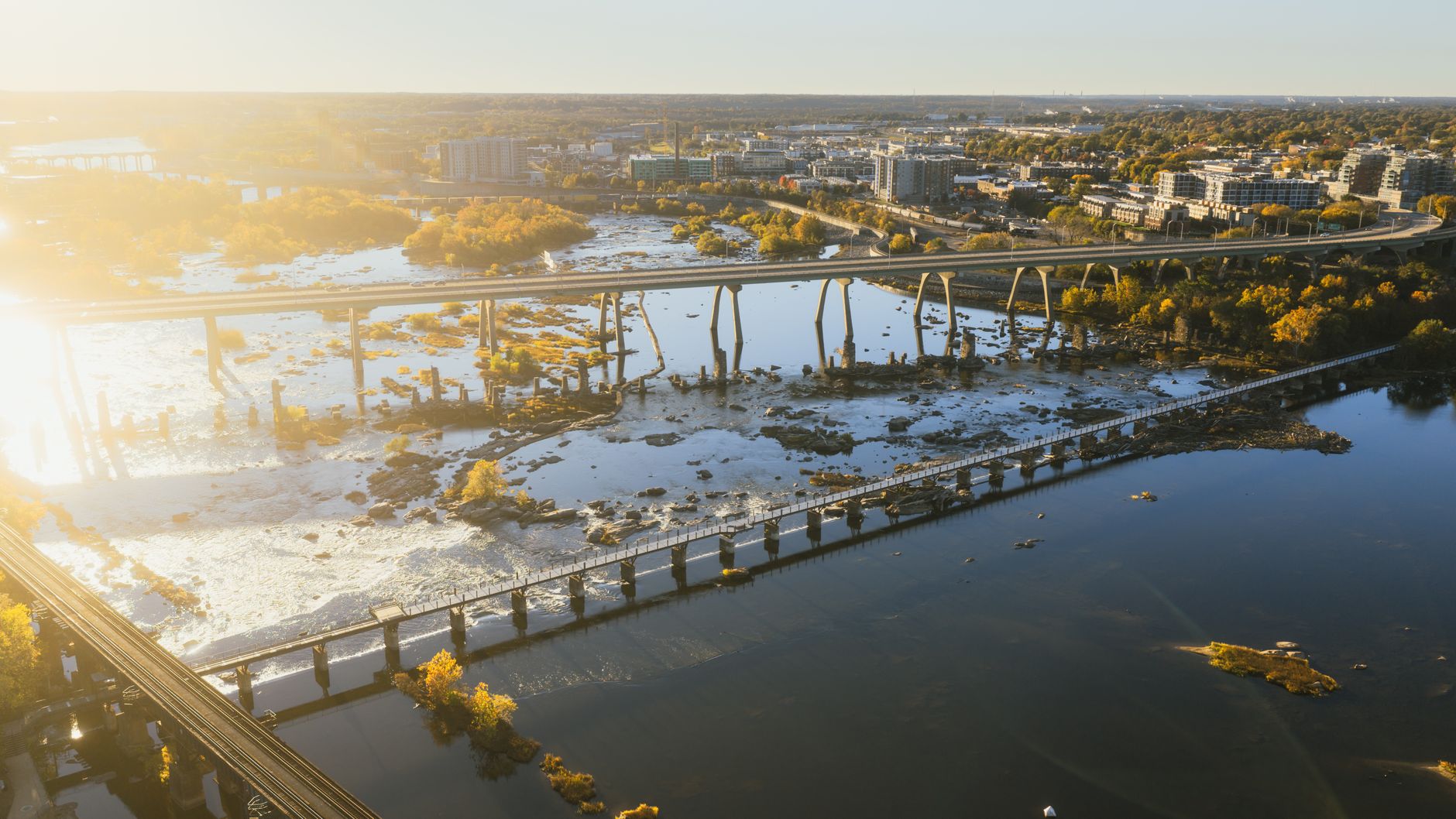 aerial view of a European urban infrastructure corridor — bridges, rail lines, and warehouse rooftops — at golden hour, with no people visible