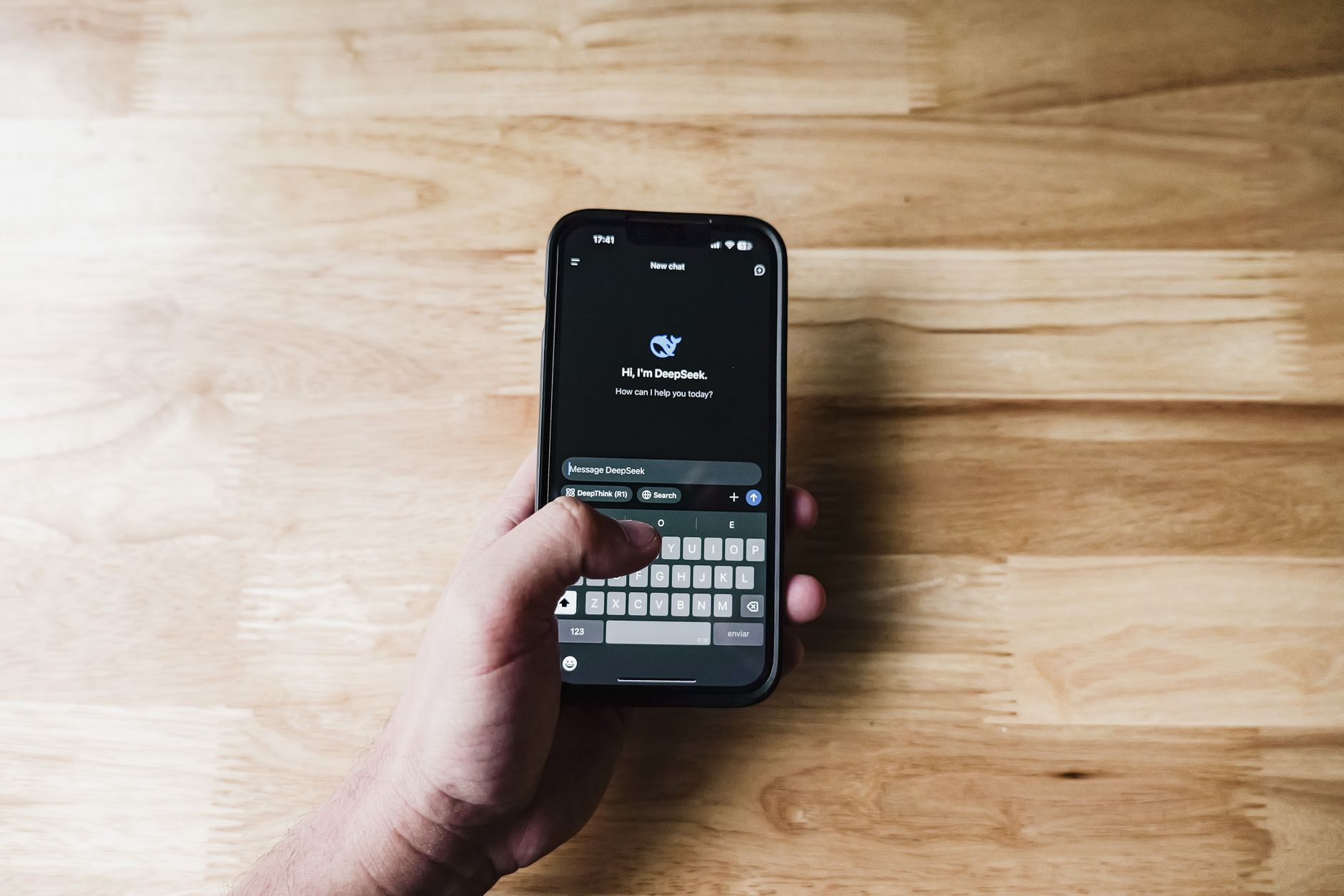 a sleek smartphone resting on a wooden desk displaying a text conversation interface, with soft natural light coming through a window beside it