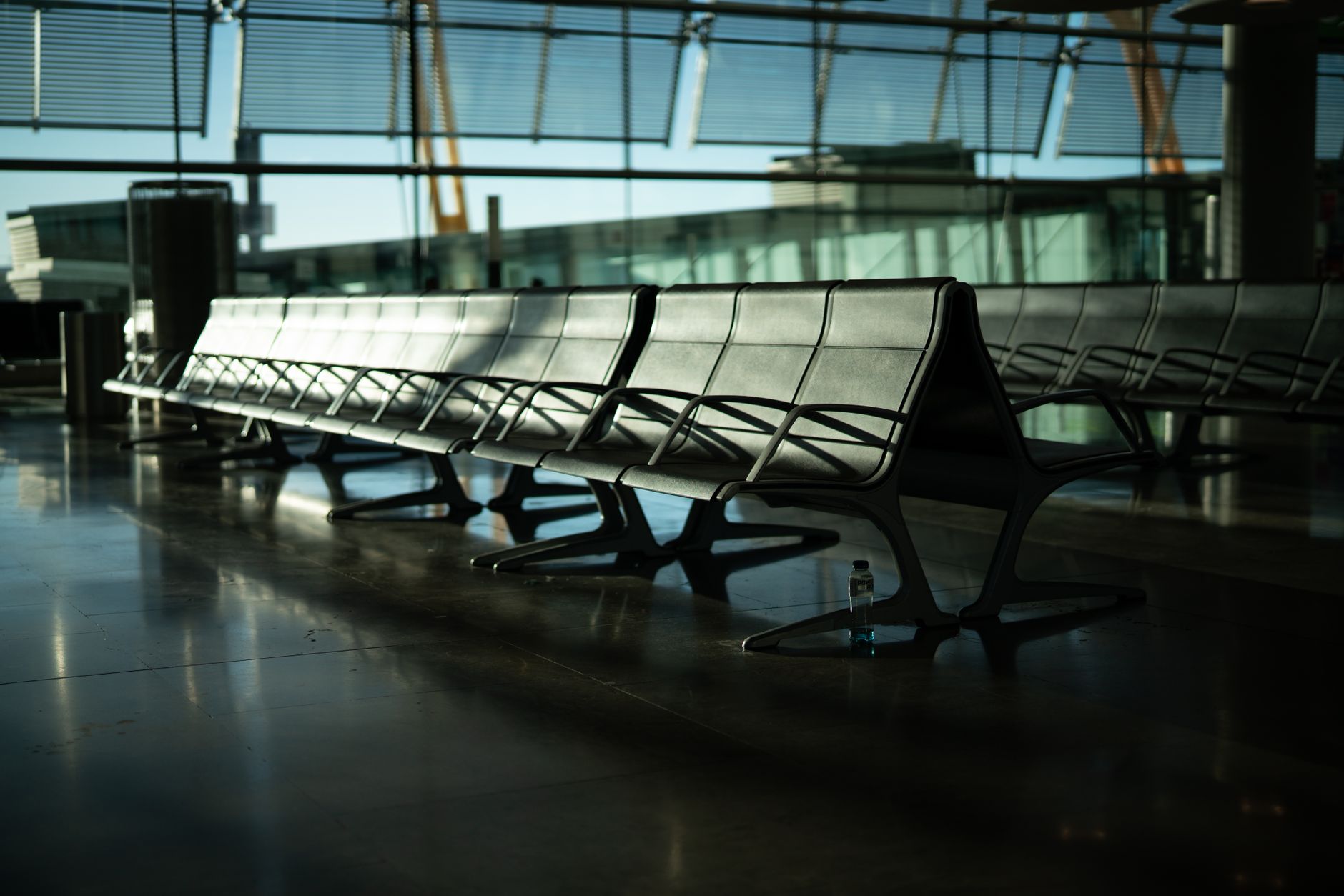 rows of empty departure gates inside a modern airport terminal with natural light streaming through floor-to-ceiling windows