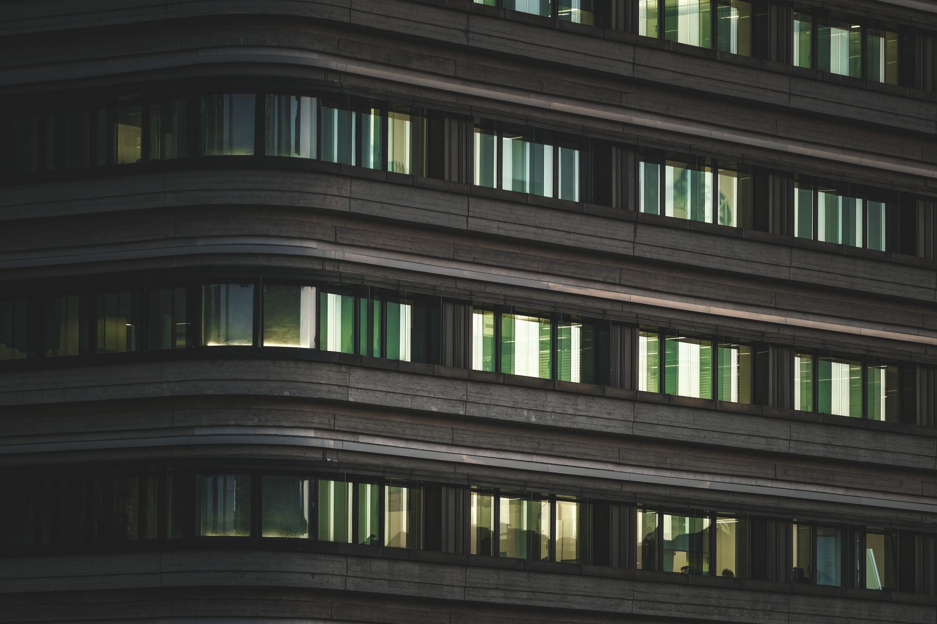 exterior of a modern glass-fronted technology office building at dusk in an urban business district, with lit windows reflecting ambient city light