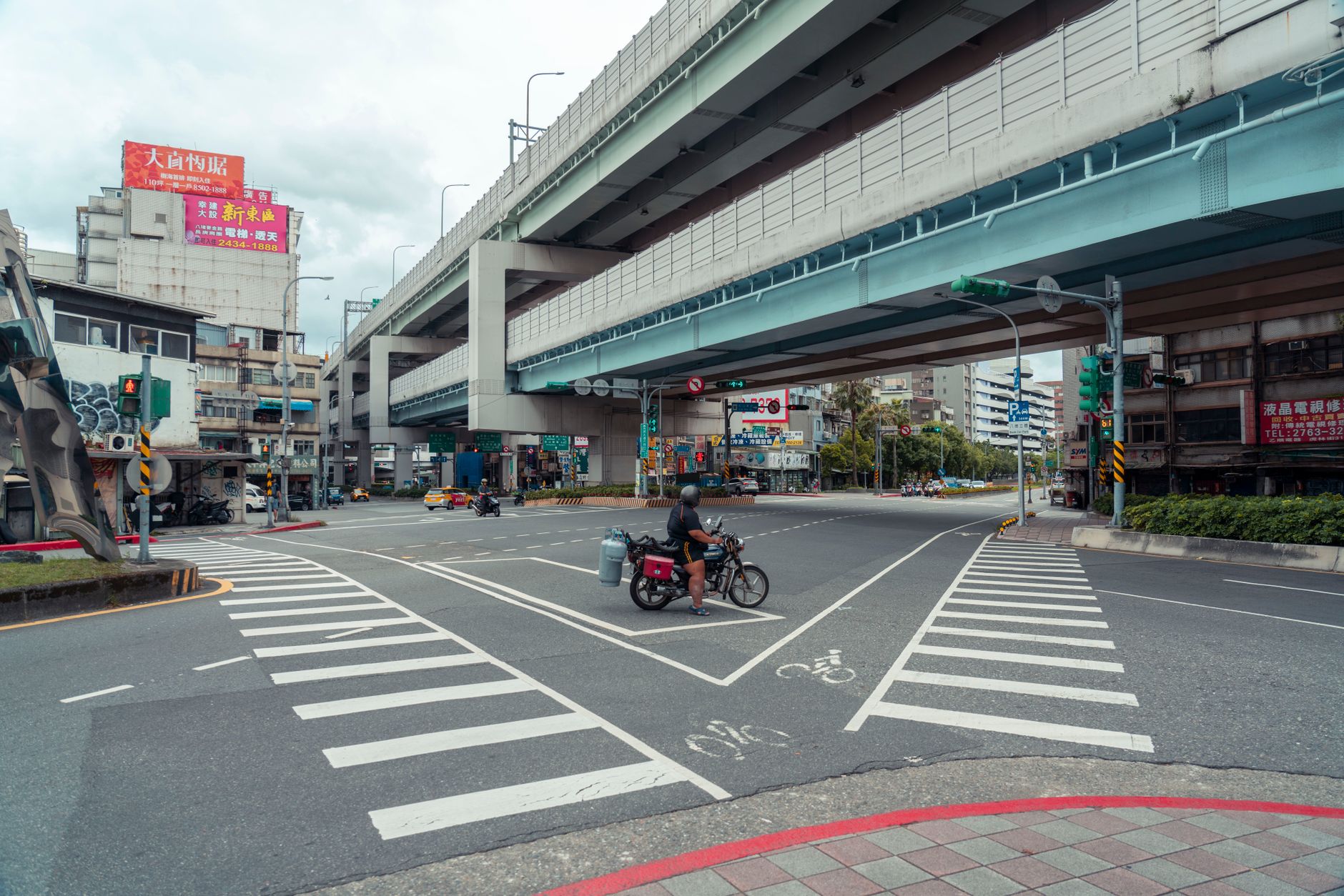 a wide shot of a busy downtown intersection with multiple lanes of traffic, overhead traffic signals, and road markings, viewed from street level with no pedestrians in focus