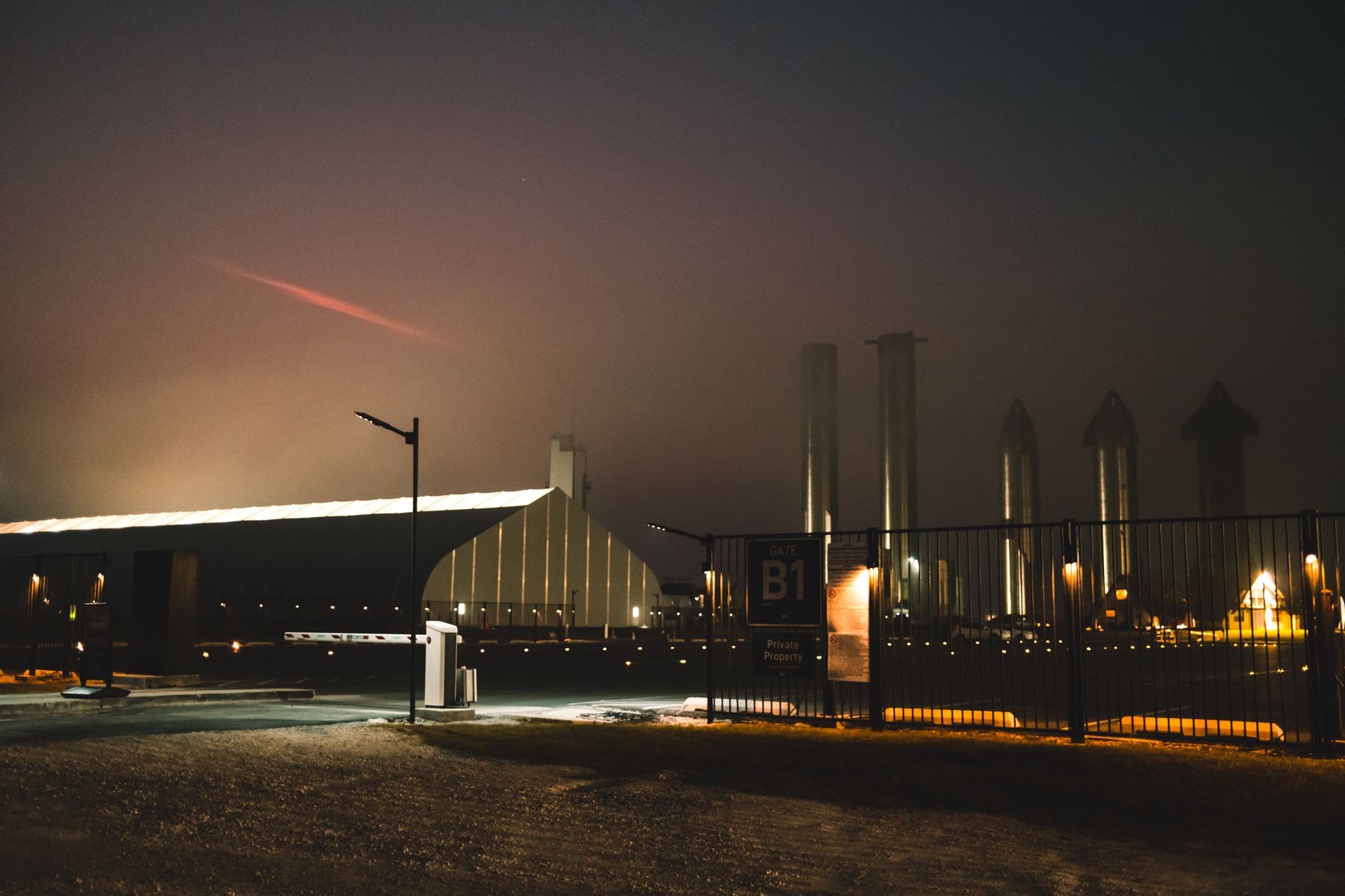 exterior of a modern data center facility at dusk, with cooling units visible along the building facade and amber security lighting illuminating the perimeter