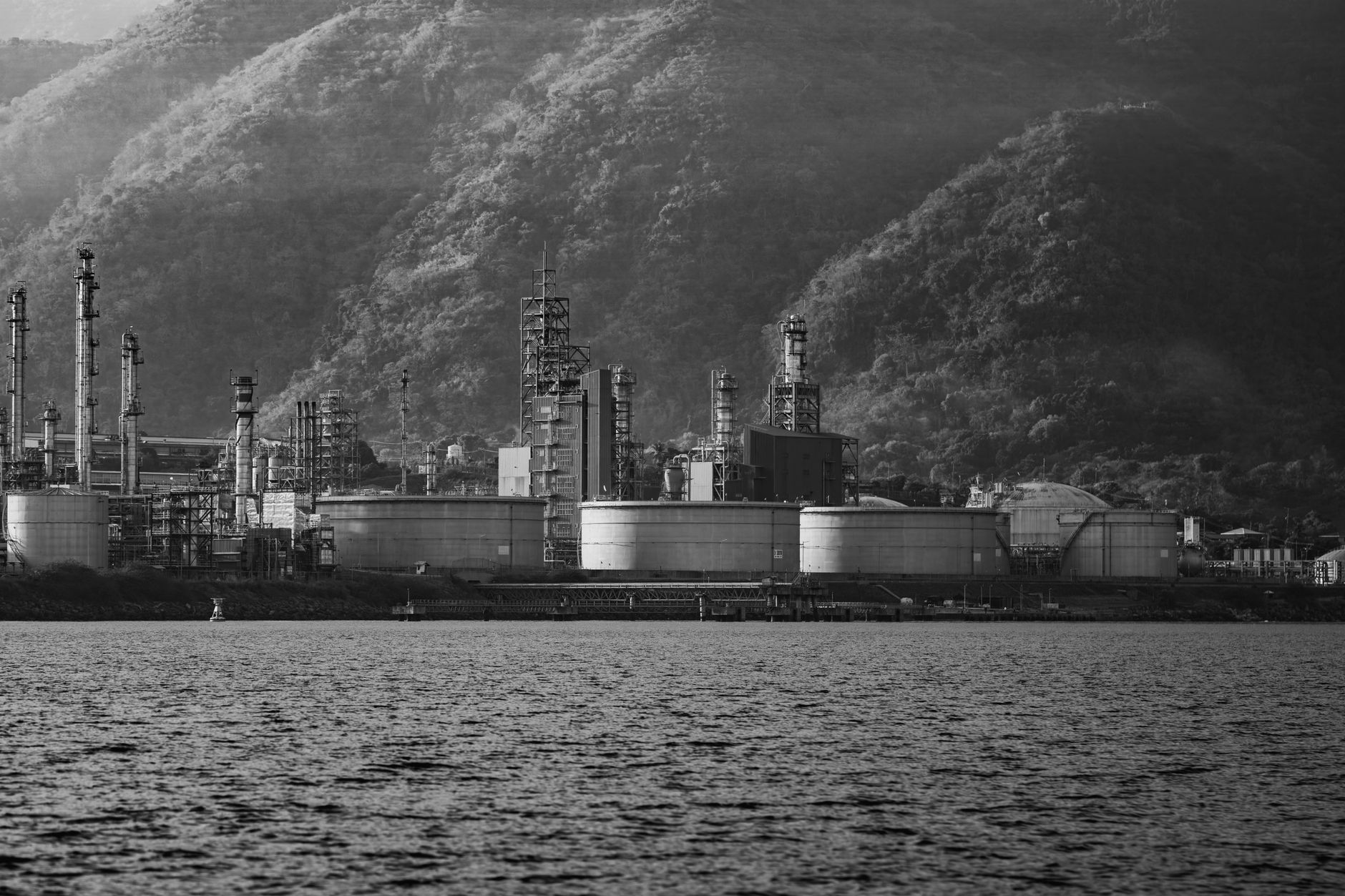 a wide aerial view of a large oil refinery complex with storage tanks and flare stacks visible at twilight, no people in frame