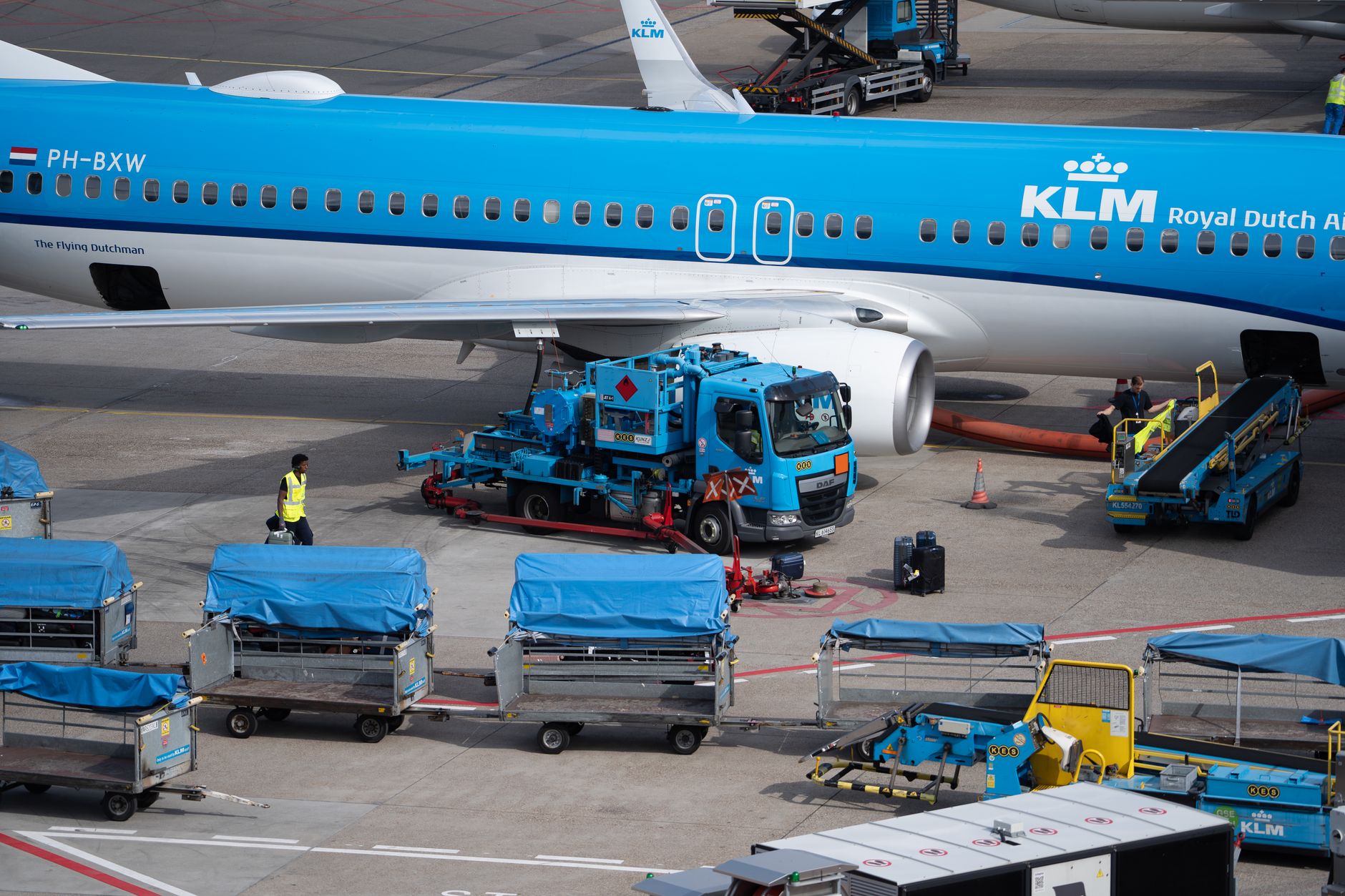 a busy commercial airport fuel truck on a tarmac beside a parked wide-body aircraft, photographed from a distance showing the fueling equipment prominently