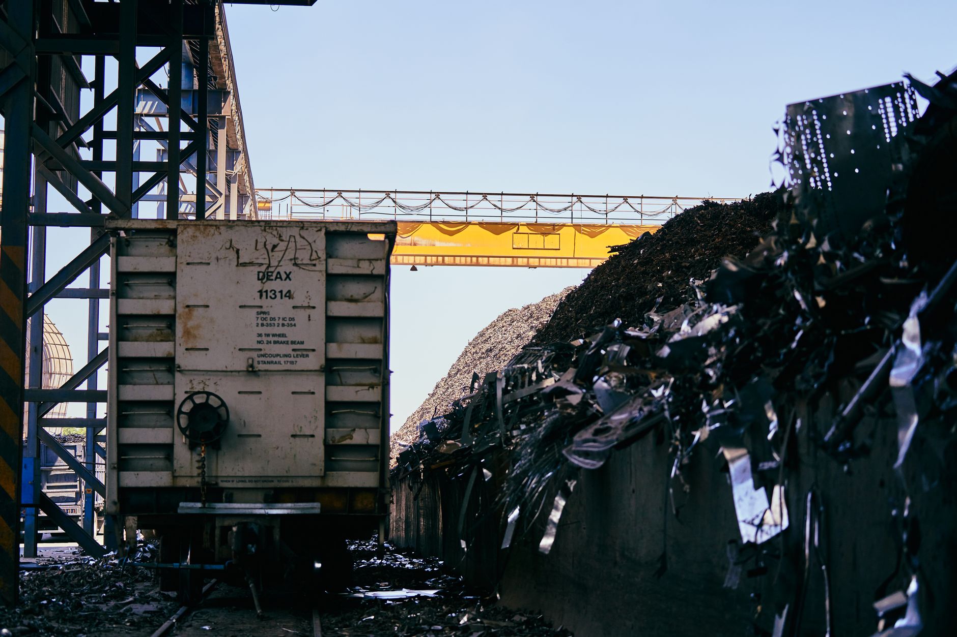 exterior of a large steel manufacturing plant at dusk, with industrial smokestacks and raw material storage yards visible in the foreground