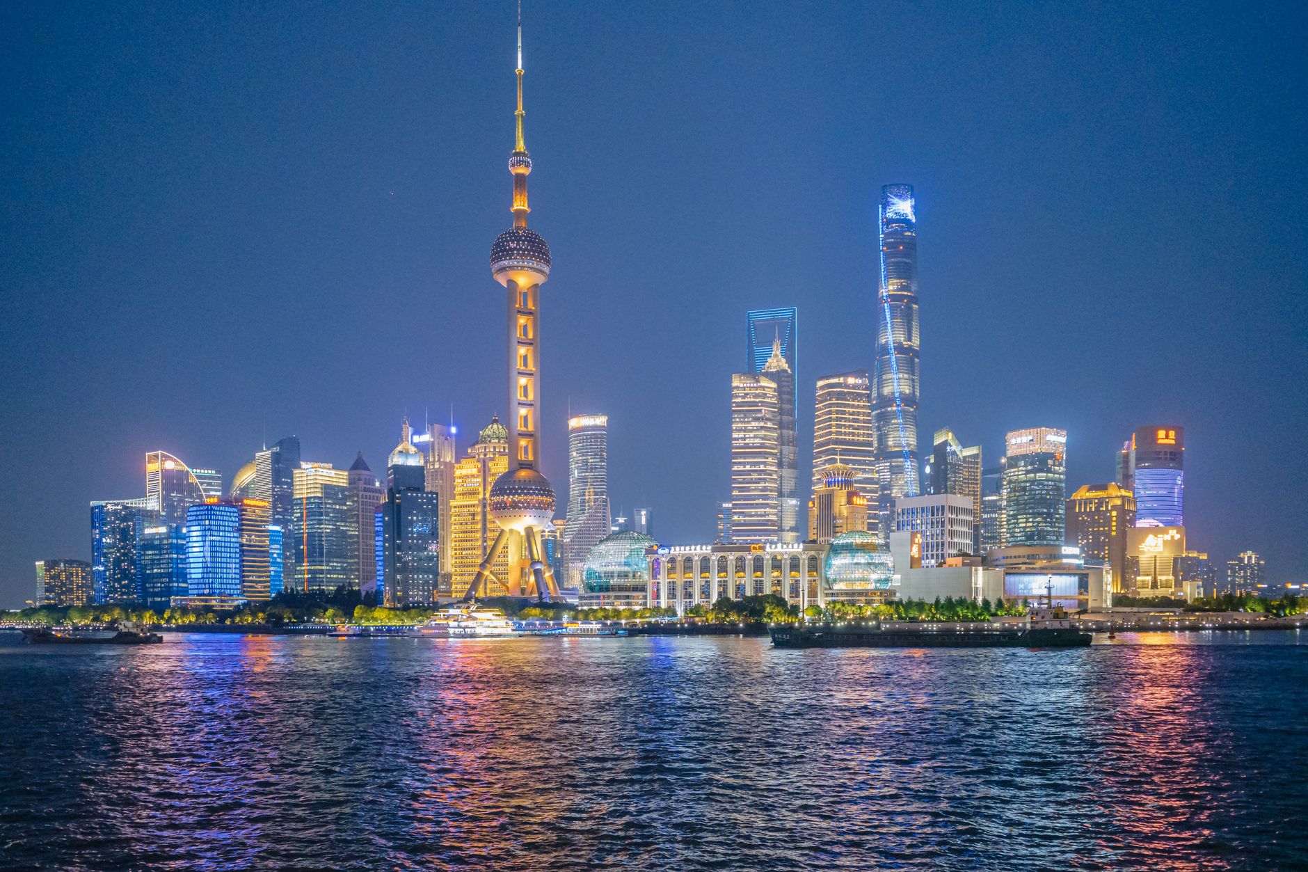 aerial view of the Shanghai financial district skyline at dusk, towers reflected in the Huangpu River with cargo ships visible in the distance
