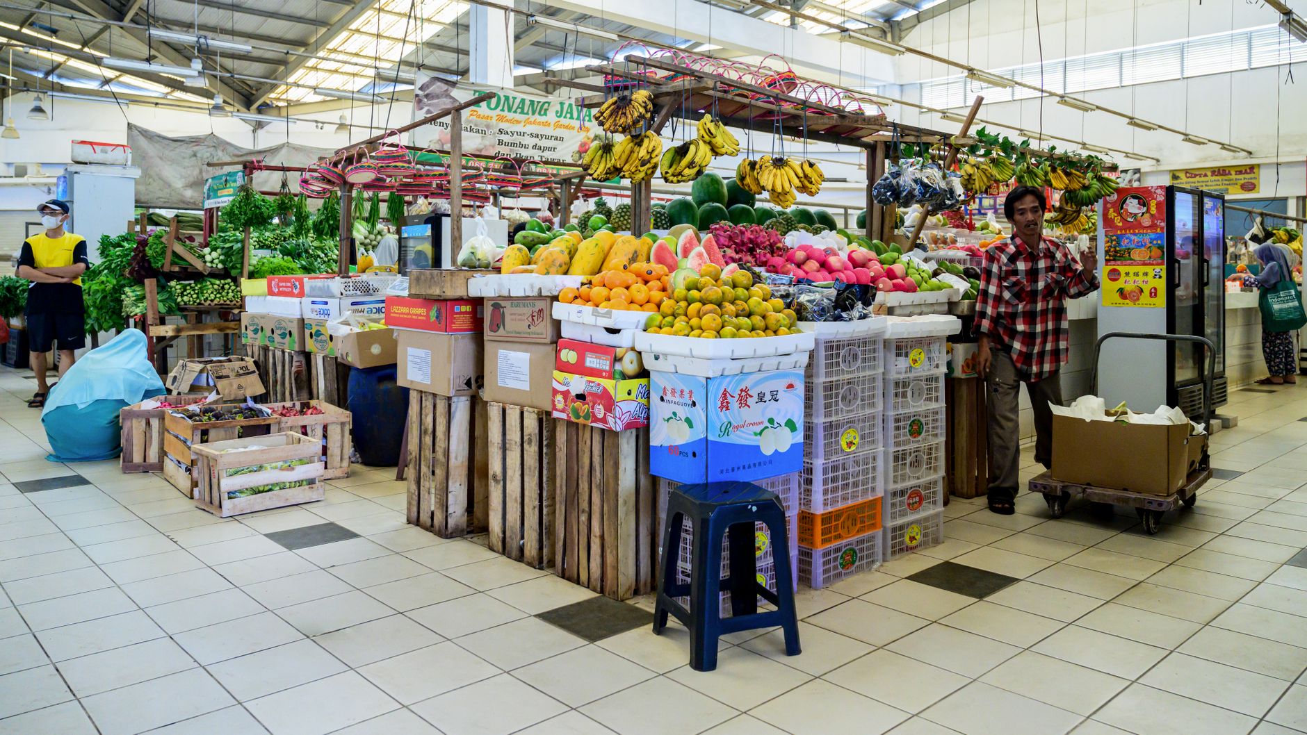 Wide-angle view of a near-empty covered wholesale food market in a large Chinese city, with rows of unoccupied vendor stalls and fluorescent overhead lighting