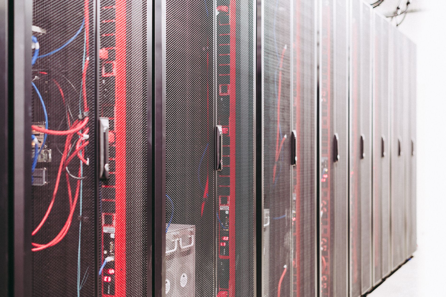 rows of densely packed server racks inside a large-scale data center, lit by blue overhead lighting with cables running along raised floor panels