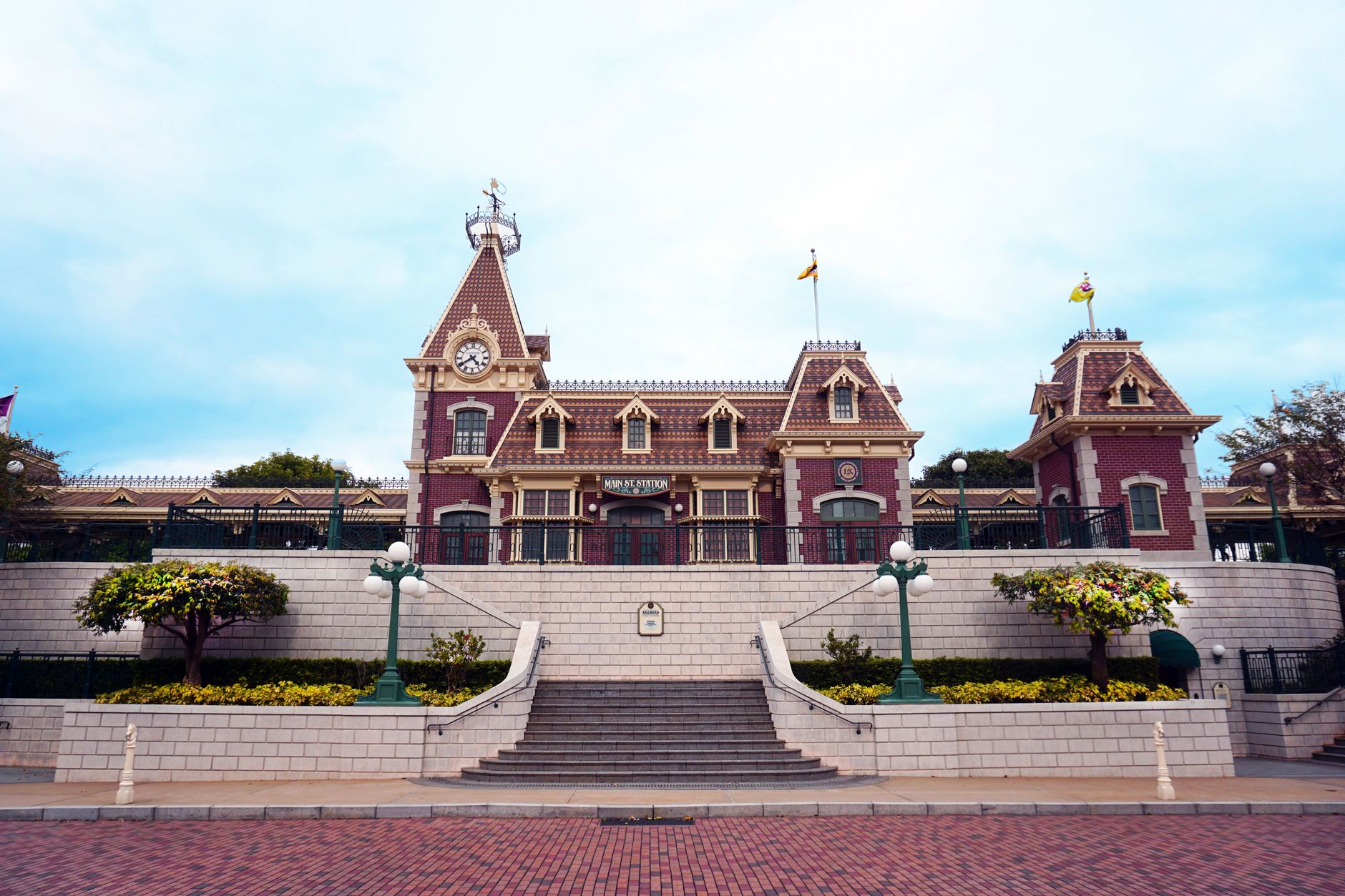 exterior of a large Disney theme park entrance at midday, with ornate archways and manicured landscaping visible in the foreground