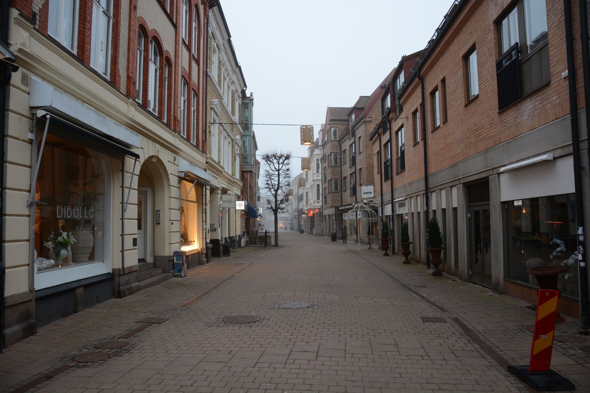 a wide-angle shot of an empty early-morning main street inside a theme park, with storefronts and decorative lampposts lining both sides of a cobblestone path