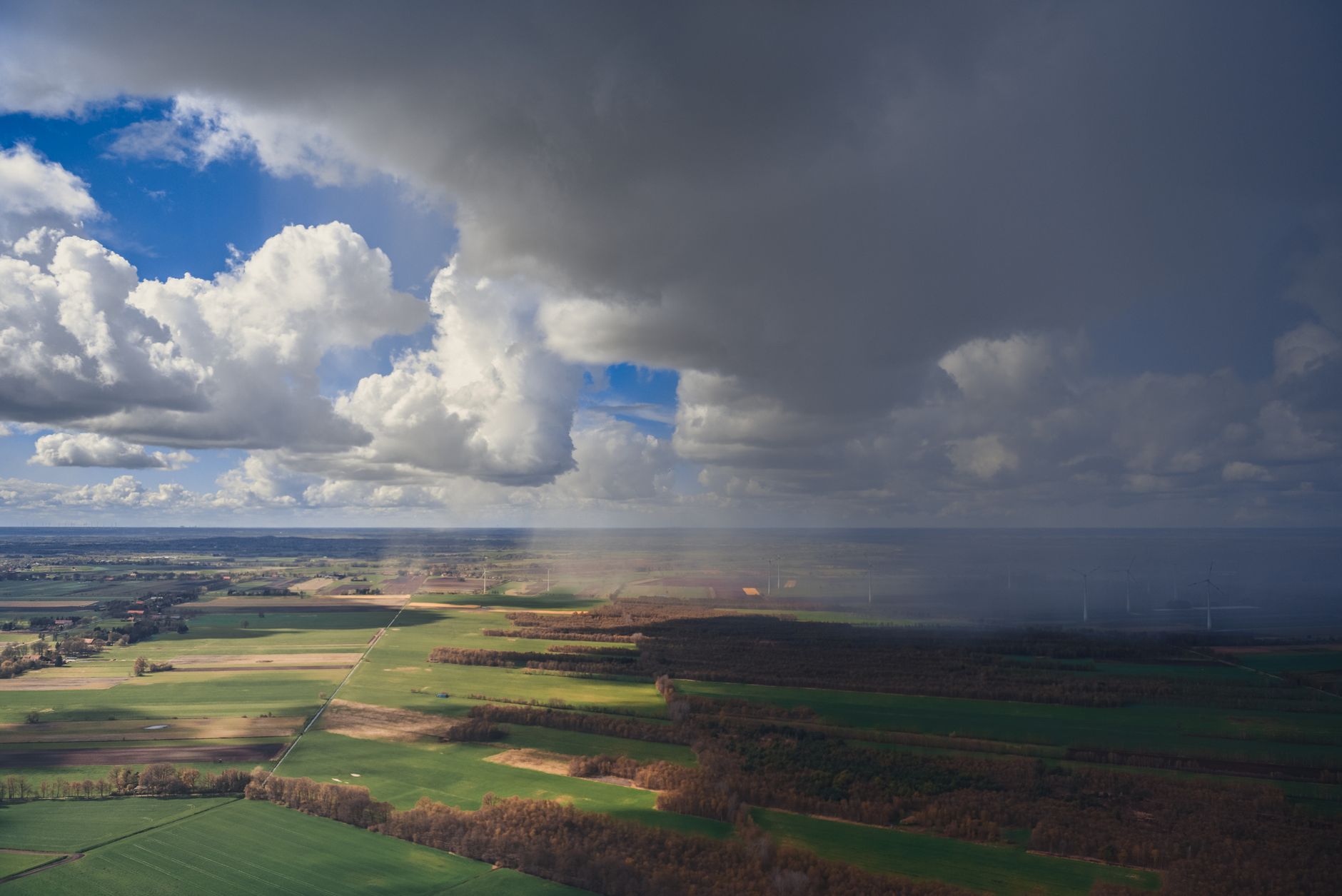 aerial view of a large industrial data center complex surrounded by open farmland and wind turbines in a flat, rural European landscape