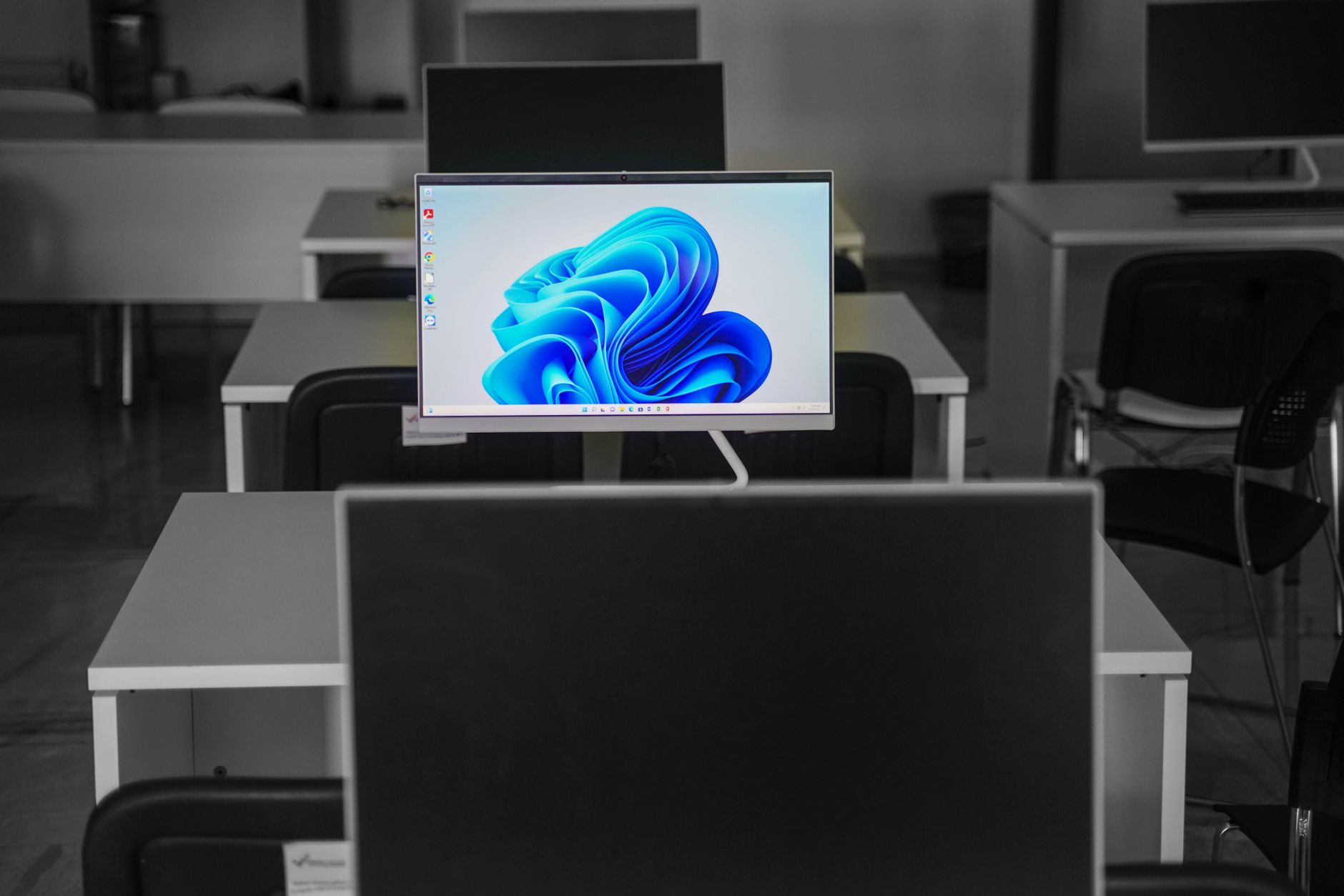 a rows of identical desktop computer screens displaying career recruitment websites in a dimly lit open-plan office, with empty chairs at each workstation