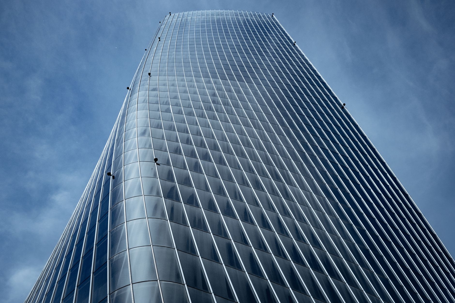 exterior view of a glass-fronted financial district office tower at midday, reflecting surrounding skyline in its facade with no visible signage