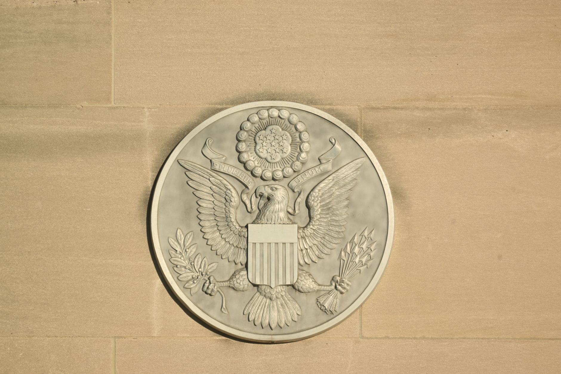 close-up of a Federal Reserve building facade with stone columns and an engraved seal, natural daylight casting sharp shadows across the stone surface
