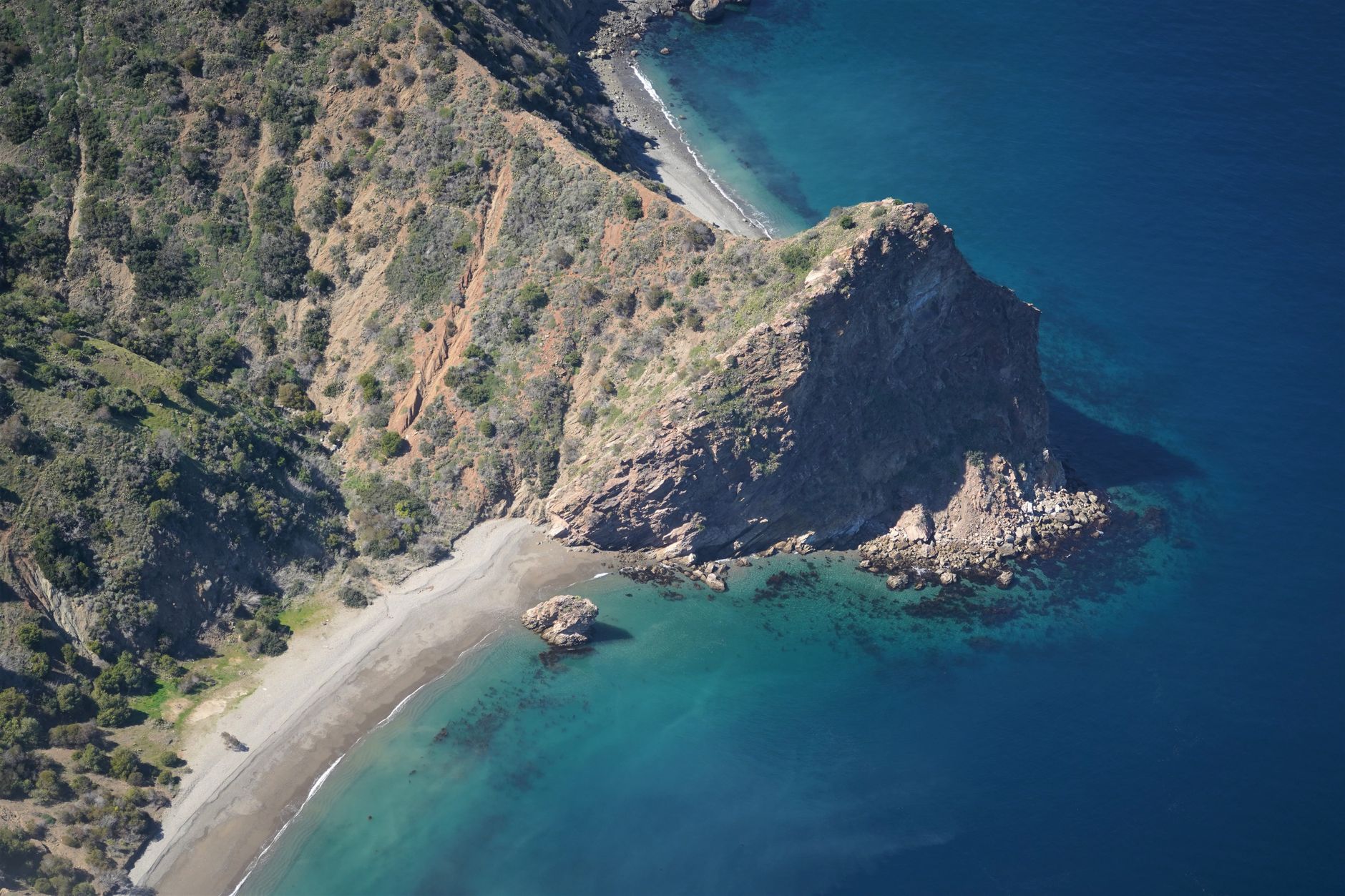 wide aerial view of a coastal radar installation on rocky Mediterranean cliffs, antenna arrays visible against a clear blue sky
