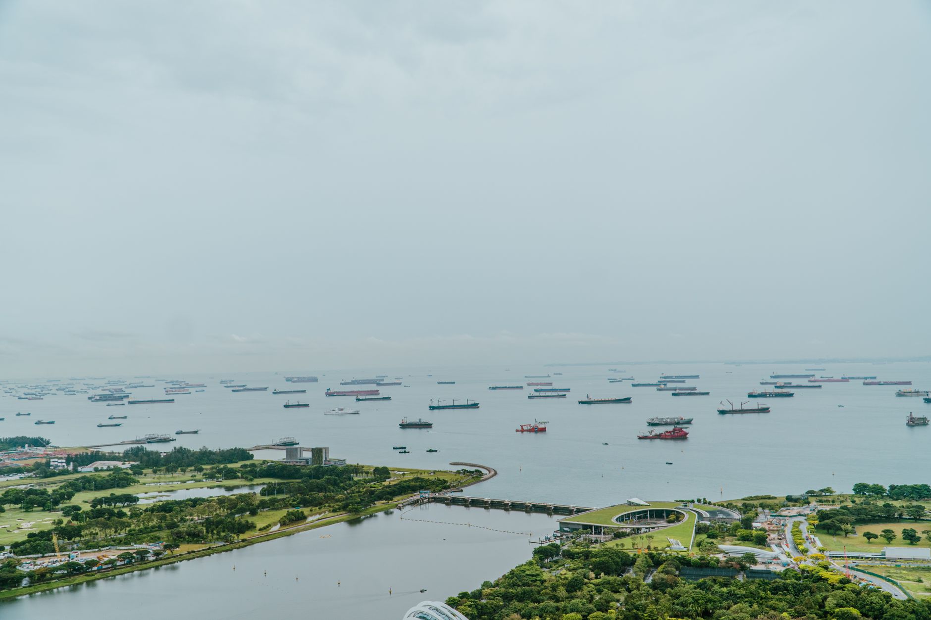 aerial view of large container ships navigating a narrow waterway surrounded by arid coastal terrain under a hazy sky