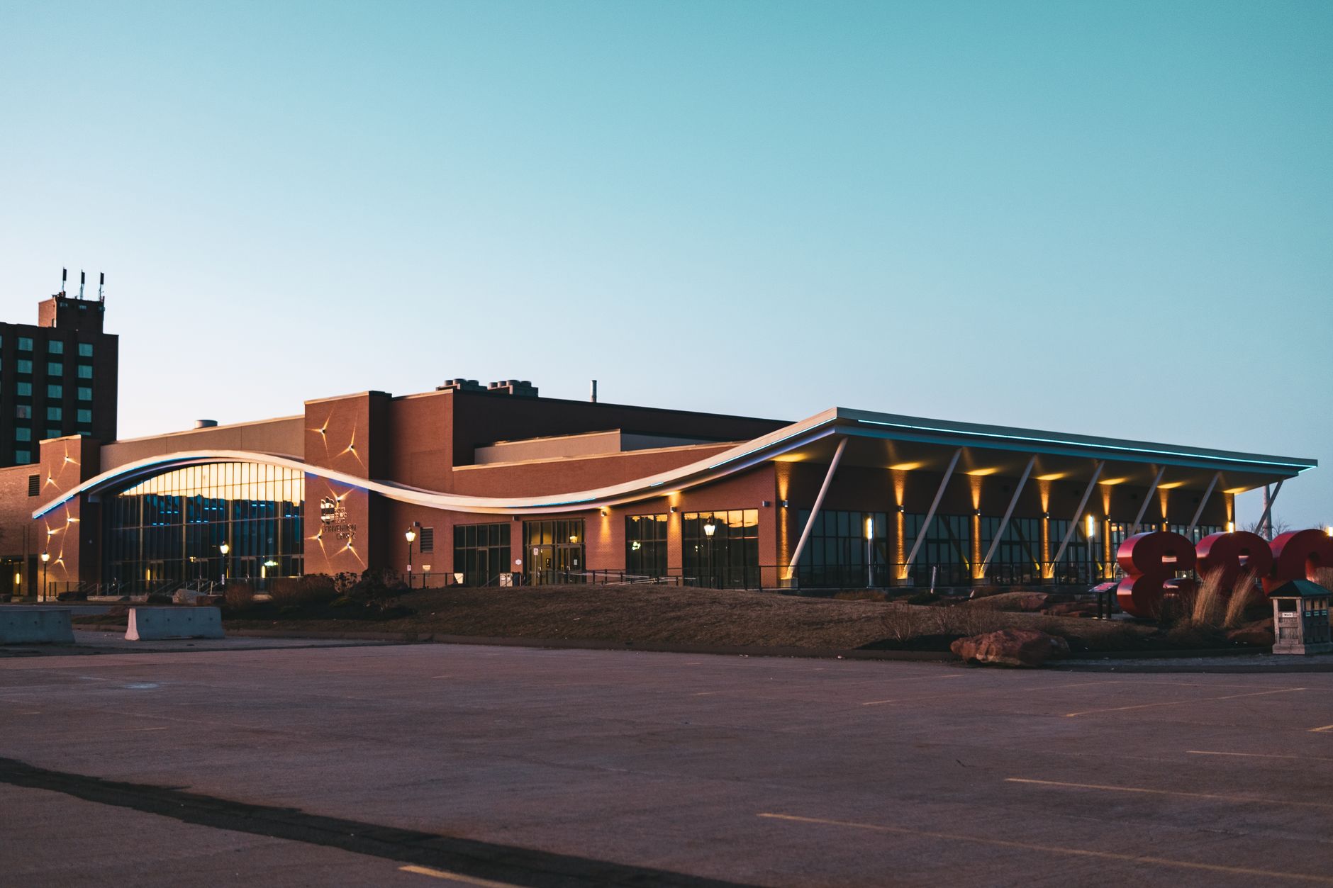 exterior of a modern pharmaceutical research campus at dusk with glass-walled buildings reflecting ambient light, cars parked in the lot below