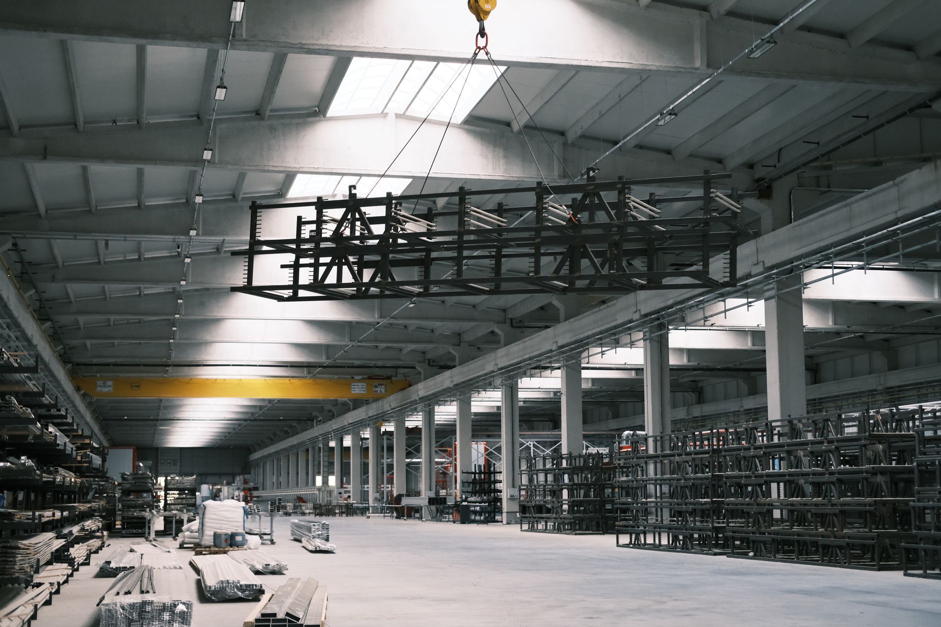 exterior of a large lithium battery cell manufacturing facility under construction in an Indian industrial zone, with steel framework and yellow construction cranes visible against a hazy sky