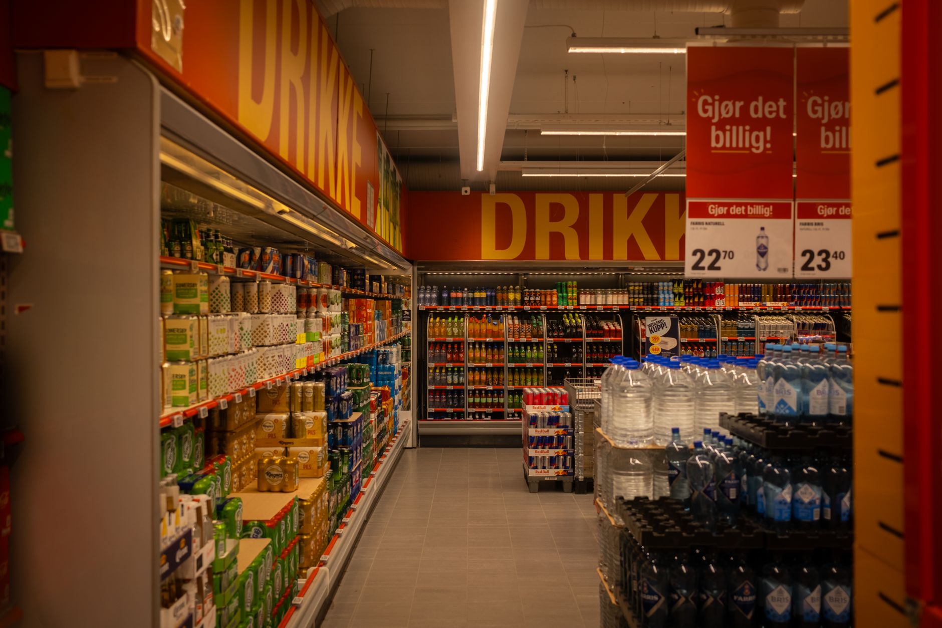 rows of empty retail shelving units inside a large discount department store under harsh overhead lighting, with price-change tags visible on several fixtures