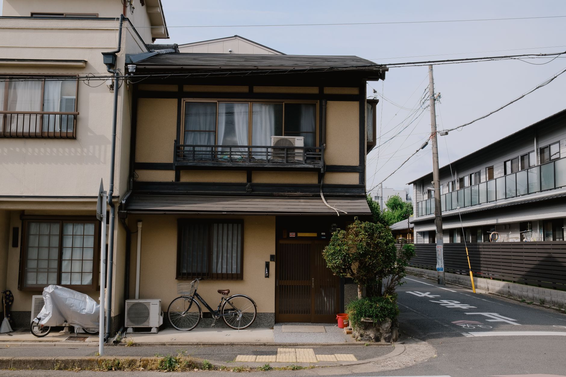 exterior of a modest two-storey rental house on a quiet suburban street, with a letterbox and a for-rent sign partially visible near the front gate