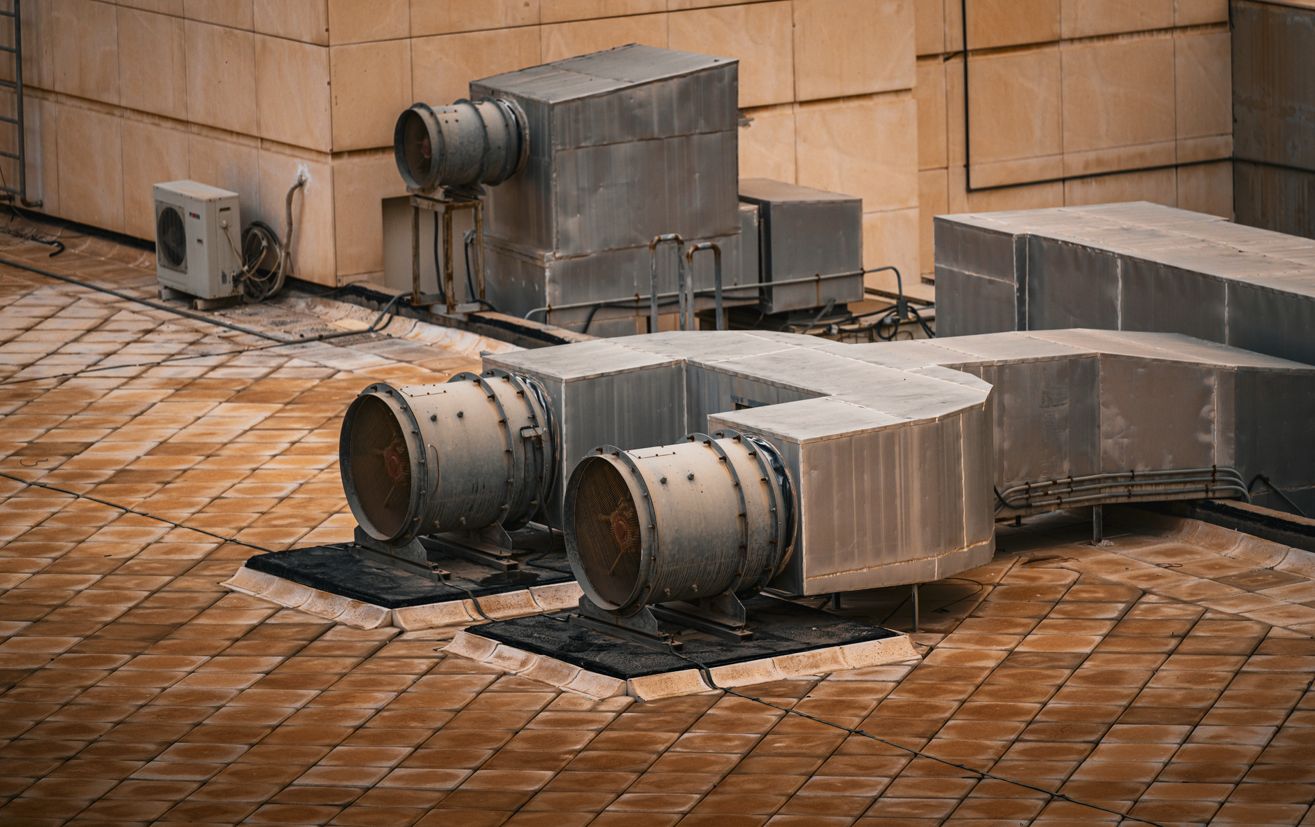 interior of a commercial HVAC mechanical room showing large ductwork, refrigeration units, and copper piping running along an industrial ceiling