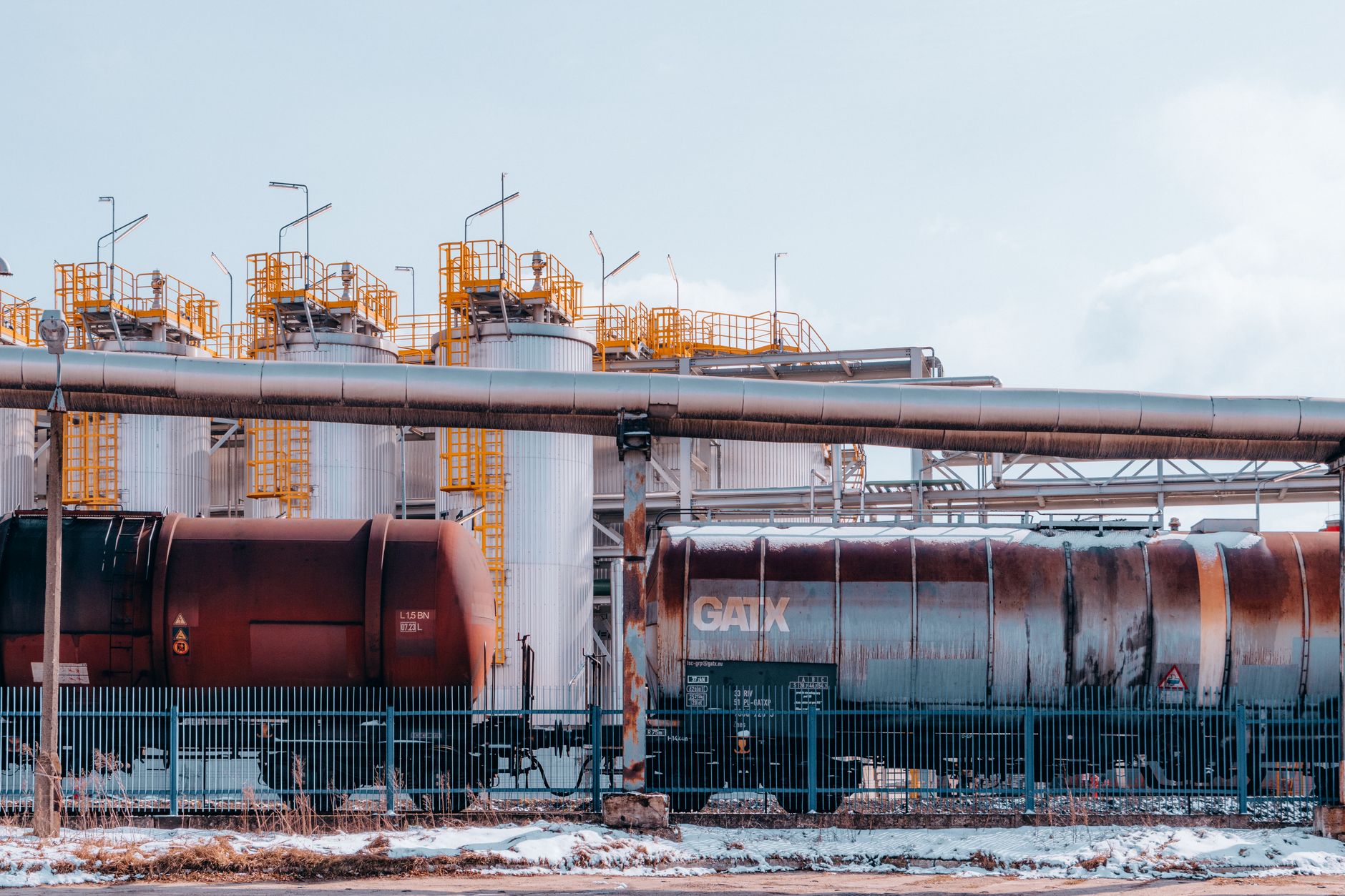 exterior view of a large oil refinery at dusk with industrial towers and pipelines visible against an orange sky