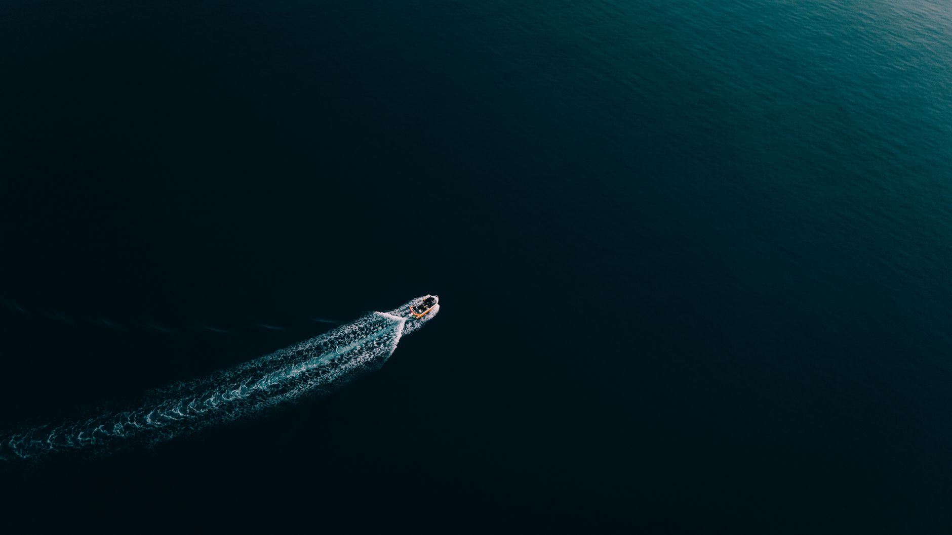 a supertanker moving through open blue waters near a narrow strait, viewed from above at wide angle with no visible faces
