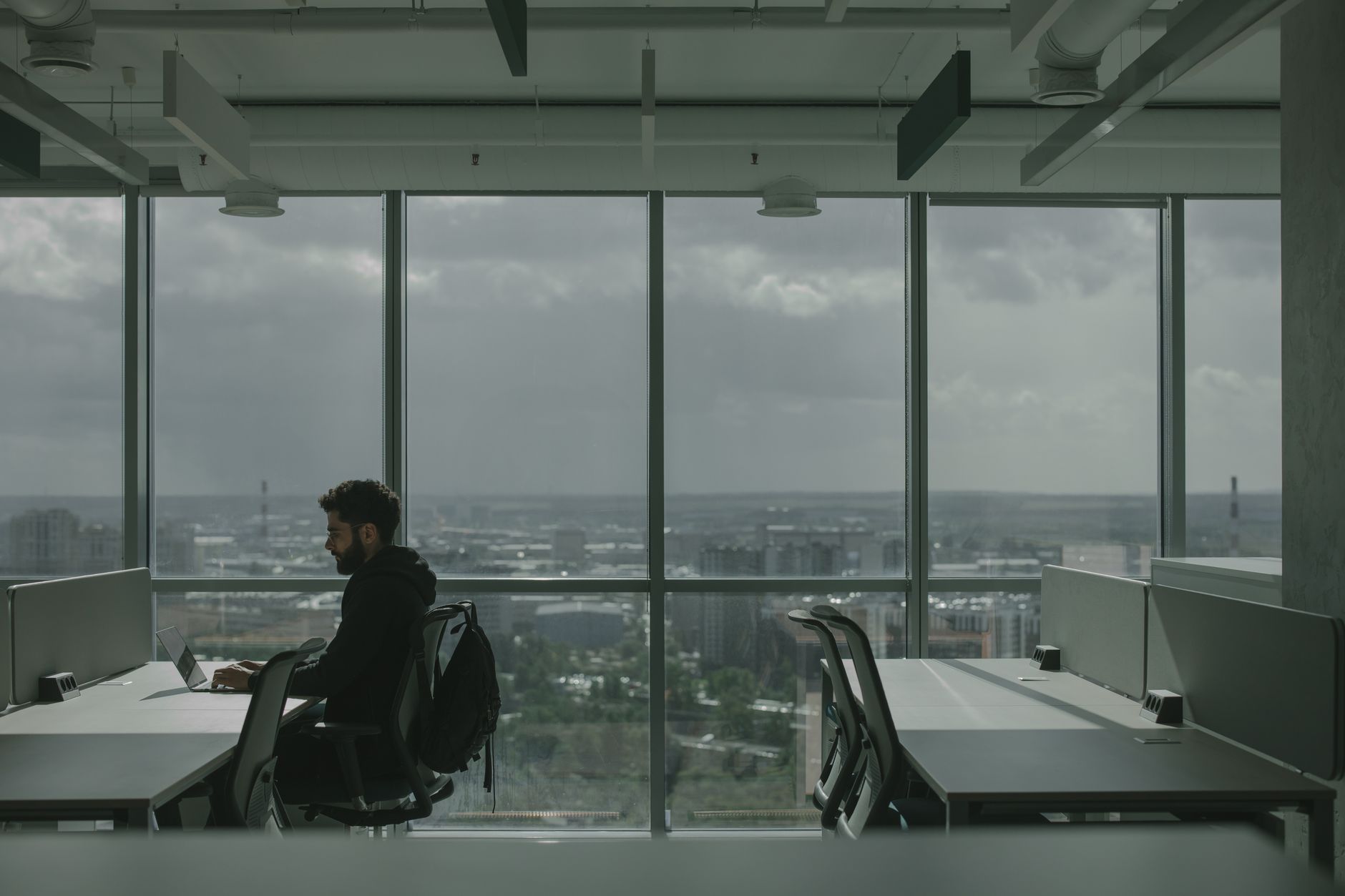 A modern co-working office interior in Tel Aviv with rows of standing desks, multiple monitors showing spreadsheets and financial models, and floor-to-ceiling windows overlooking an urban skyline